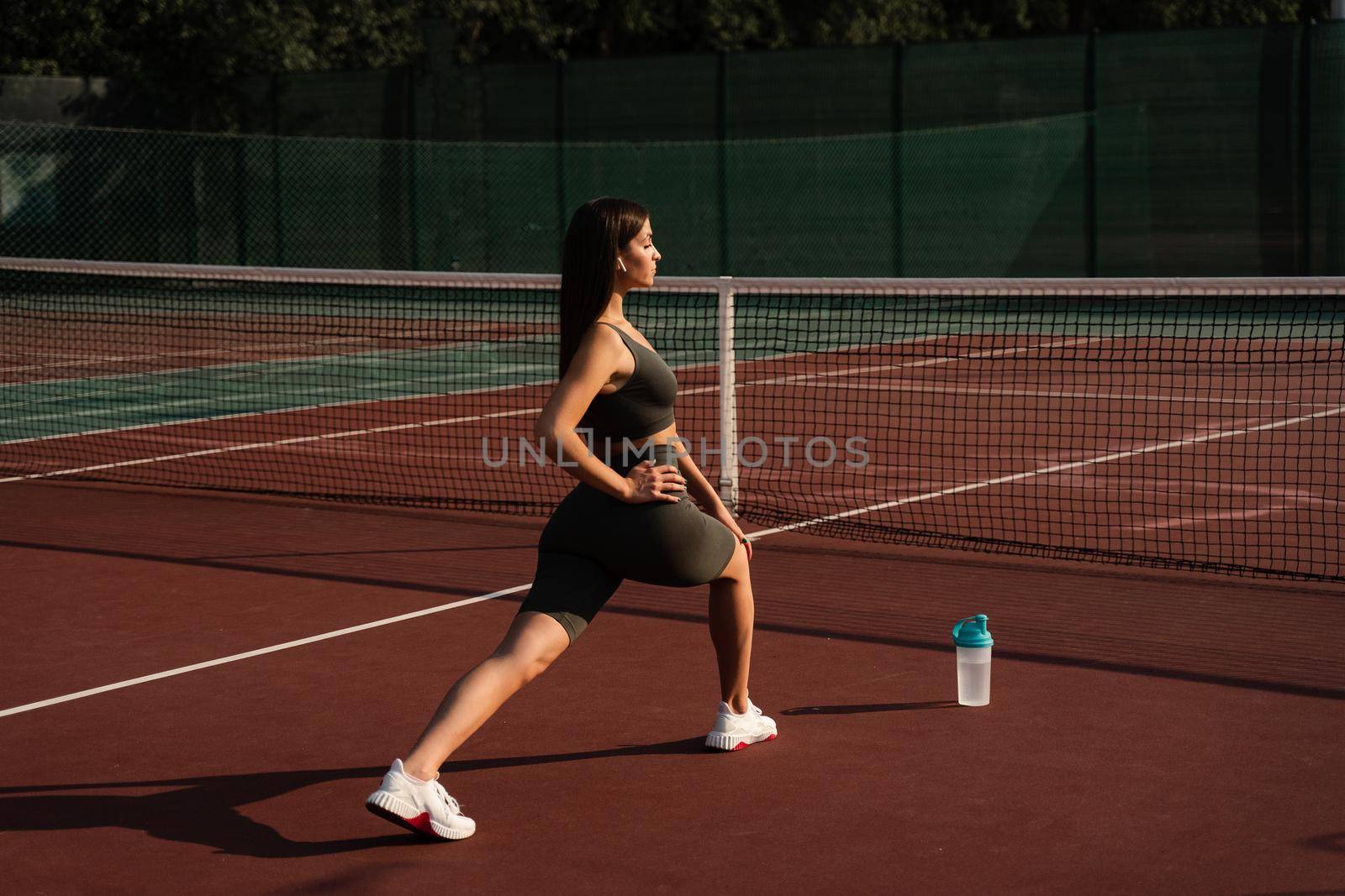 Fit attractive girl dressed in sportswear is training outside. Young woman doing lunges outdoors