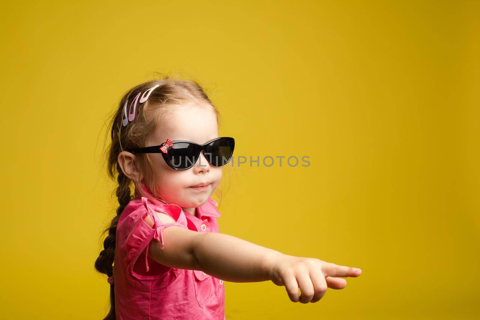 Little girl in dress and sunglasses indicating the direction. by StudioLucky