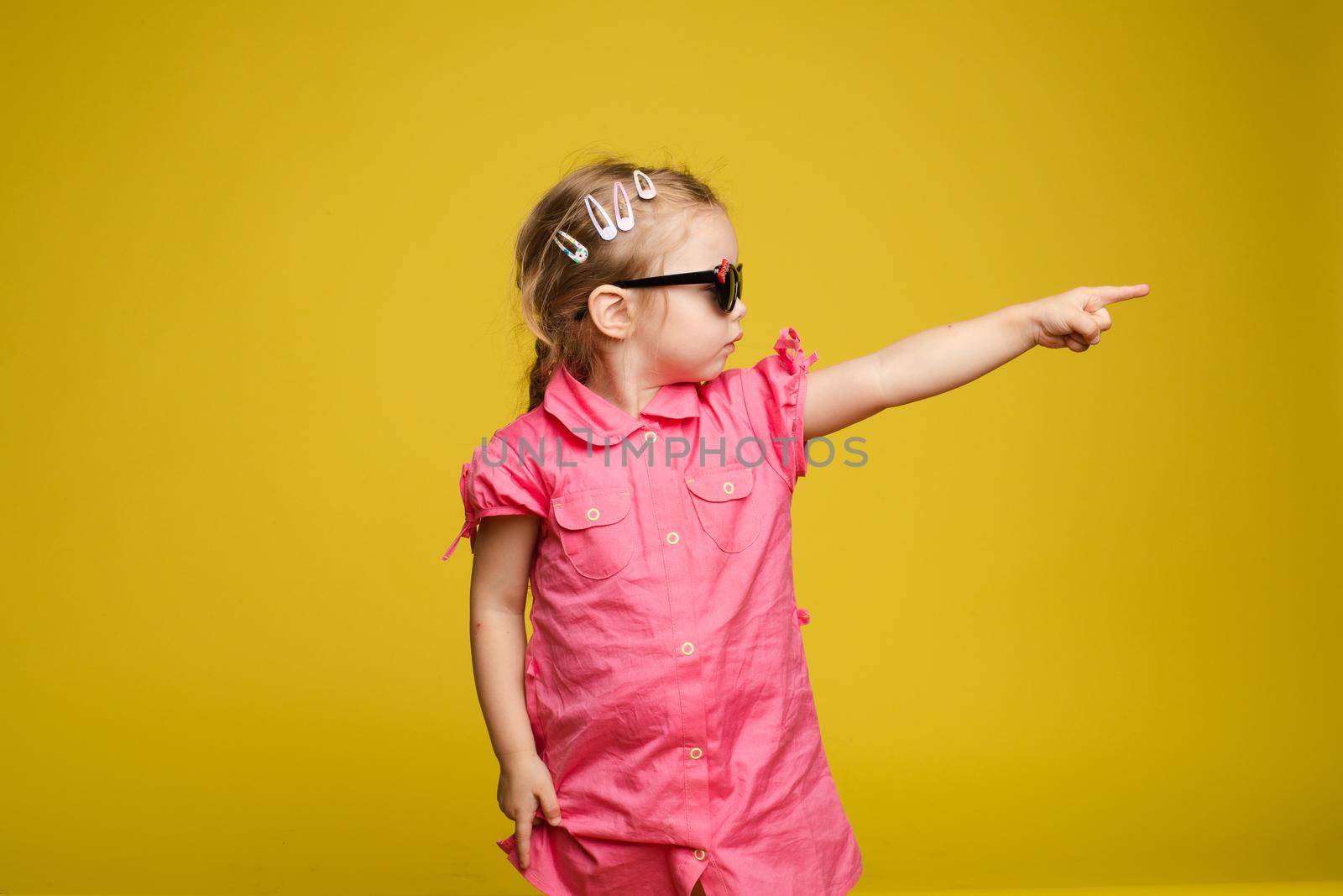 Little girl in dress and sunglasses indicating the direction. by StudioLucky