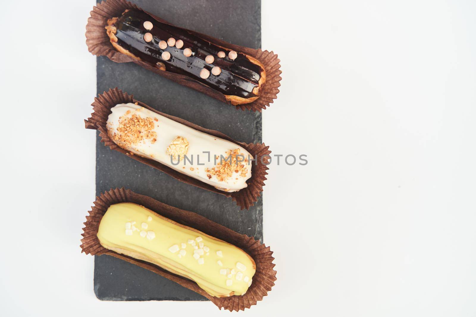 Three eclairs on a black tray top view. Traditional French dessert