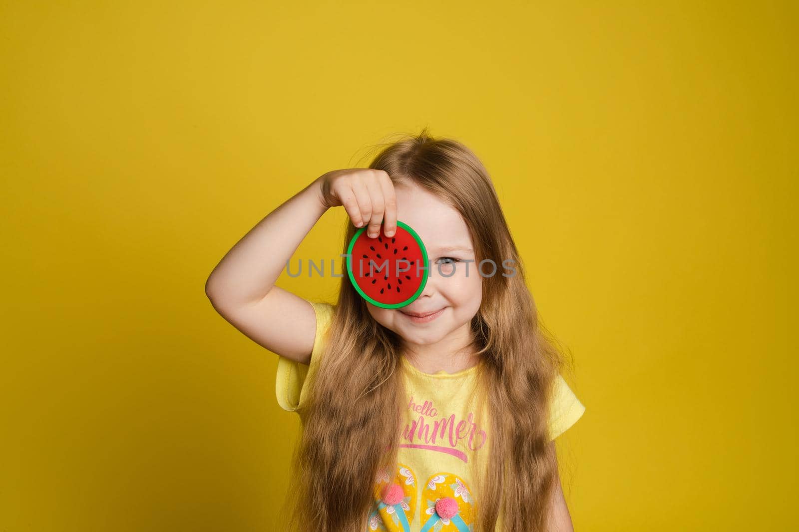 Portrait of smiling little girl holding slice of lemon near eye looking at camera medium close-up by StudioLucky