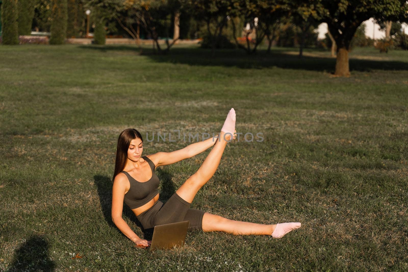 Active fit girl training online with laptop on green grass in the park. Sport lifestyle. Outdoor training