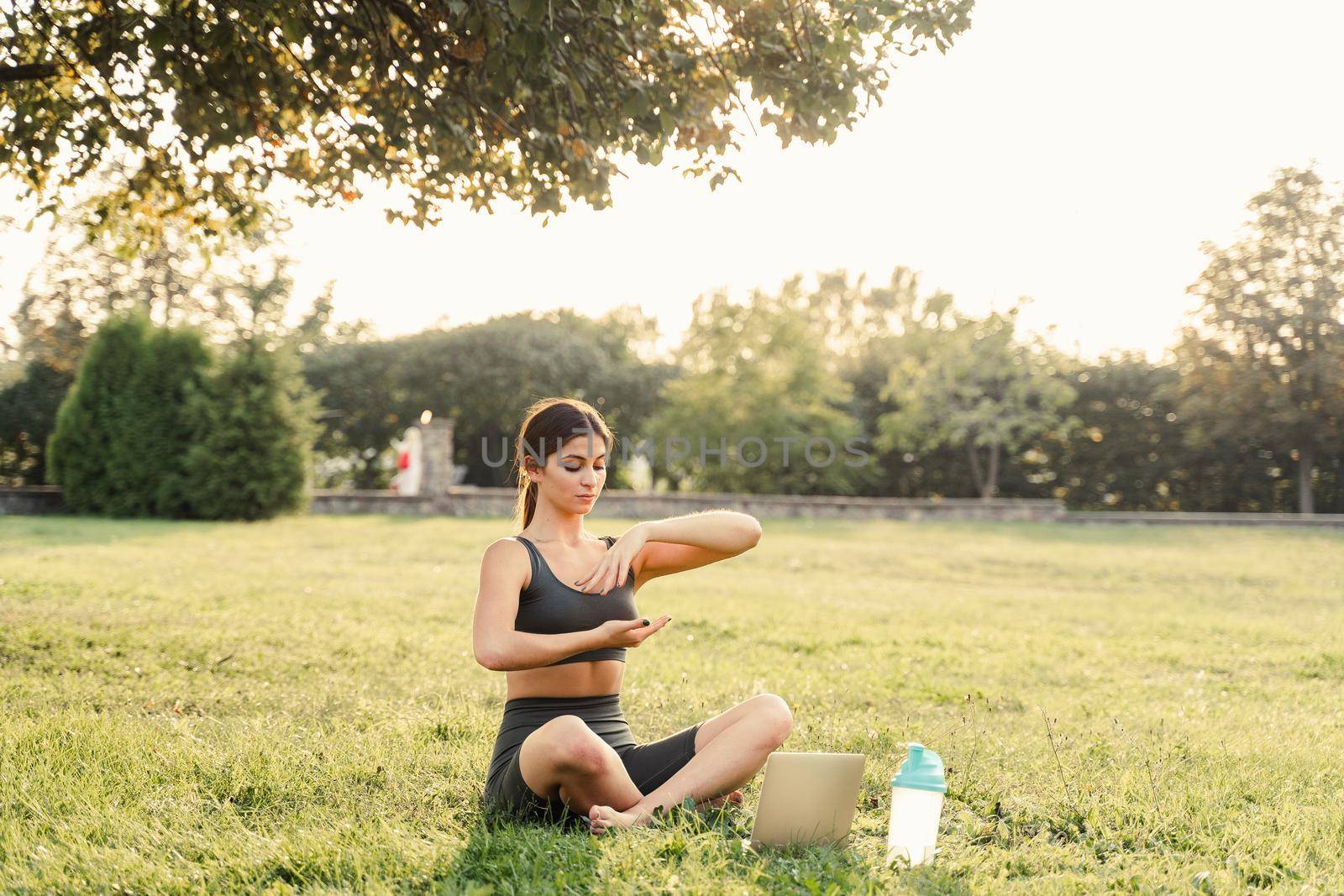 Qigong chinese meditation online with laptop in green park. Sport training outdoor. Fit asian girl is meditating outside. by Rabizo