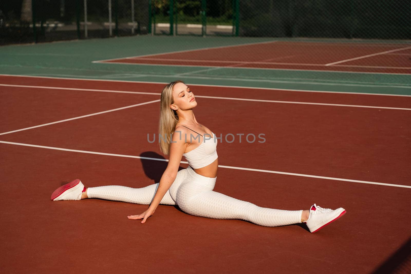 Fit blonde girl does front leg spirit workout exercise outdoor. Attractive girl trains outside. Sports lifestyle. by Rabizo