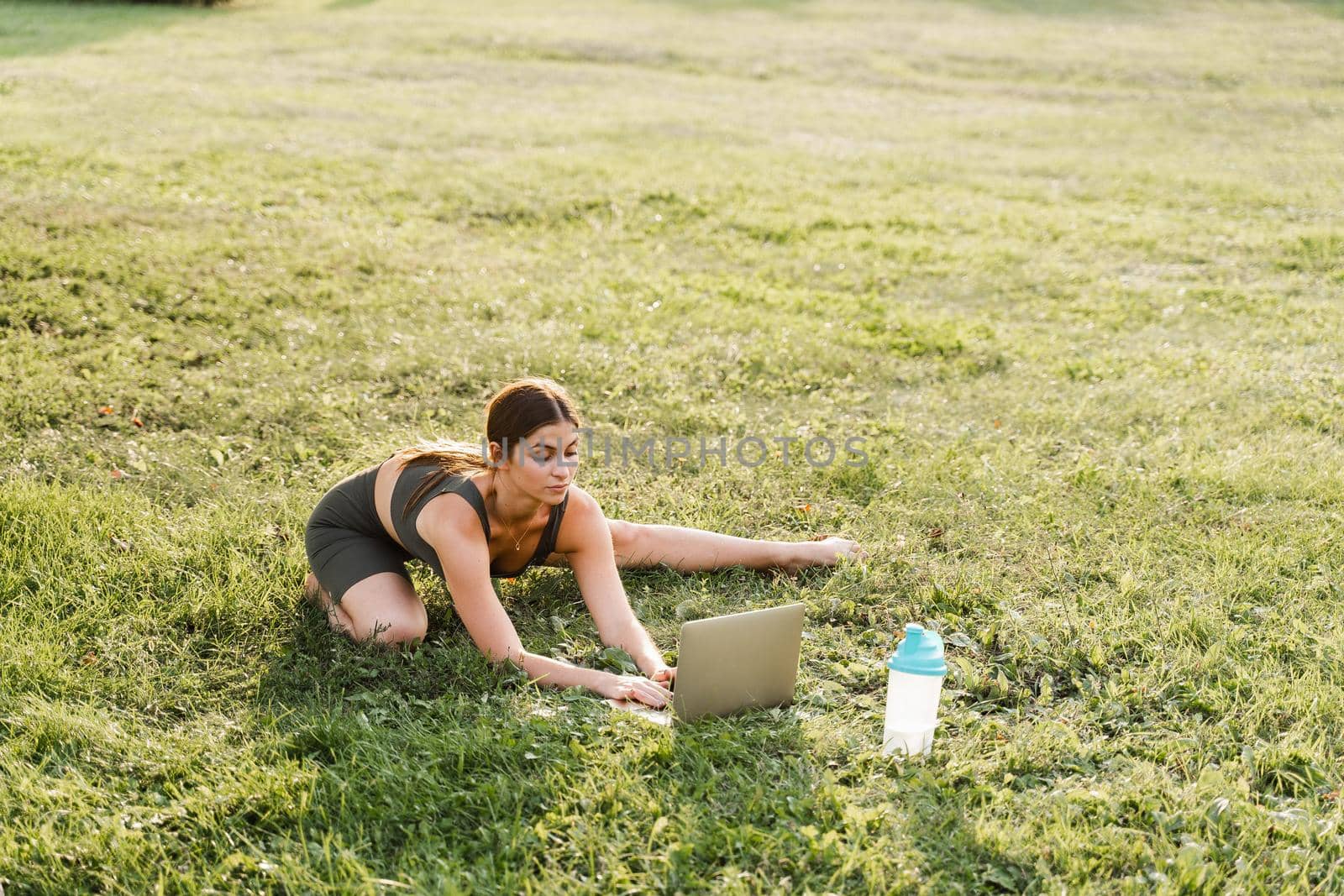 Fit girl with laptop on the green grass. Fitness trainer is chatting online with clients and explain exercises. Sport lifestyle