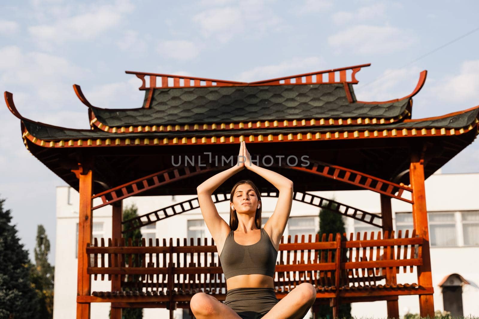 Praying and meditation in lotus position. Fit girl is sitting and meditating outdoors near chinese gazebo. by Rabizo