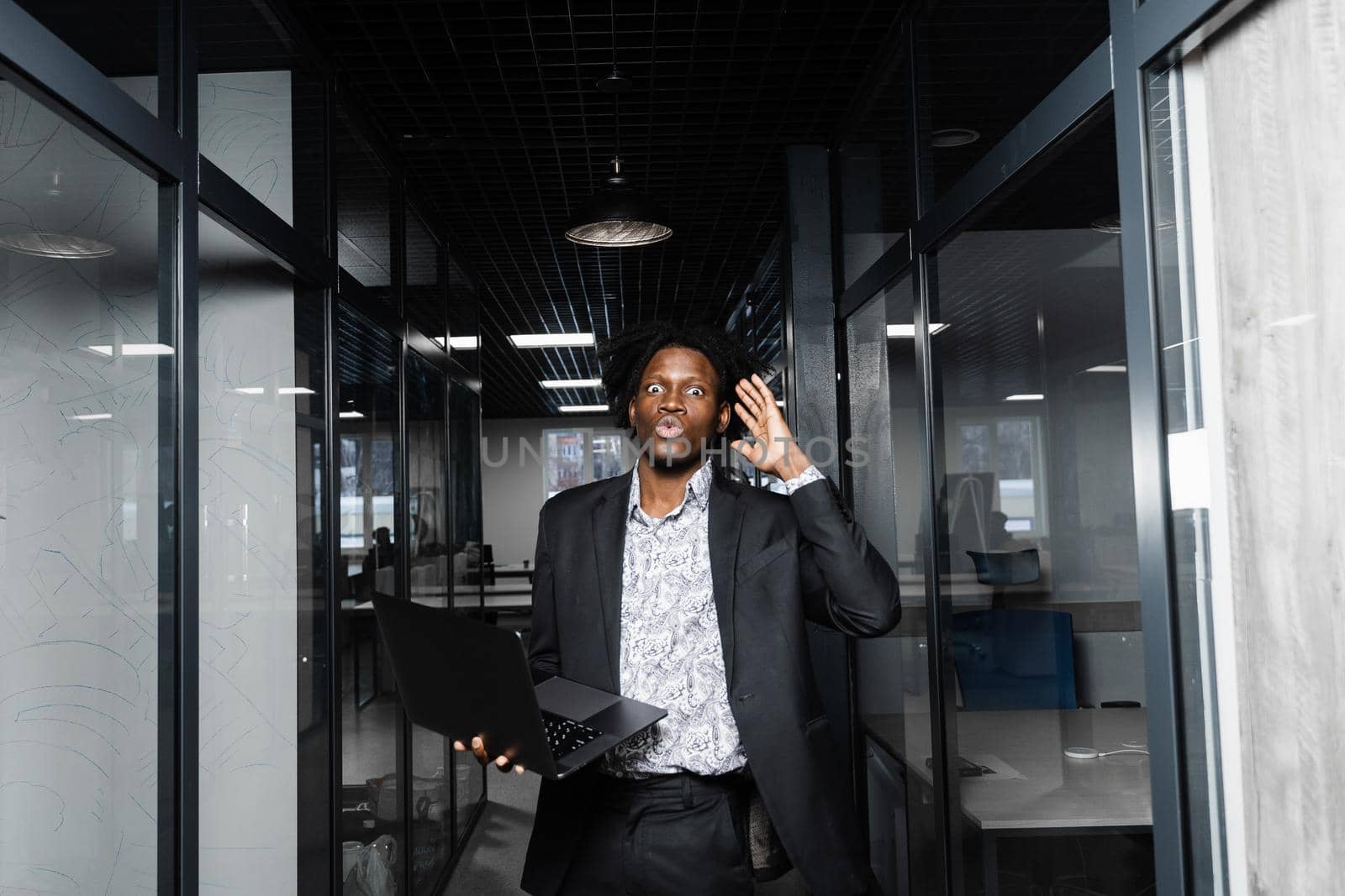 Surprised black man with laptop in the office. Shocked emotional handsome african business man in coworking space