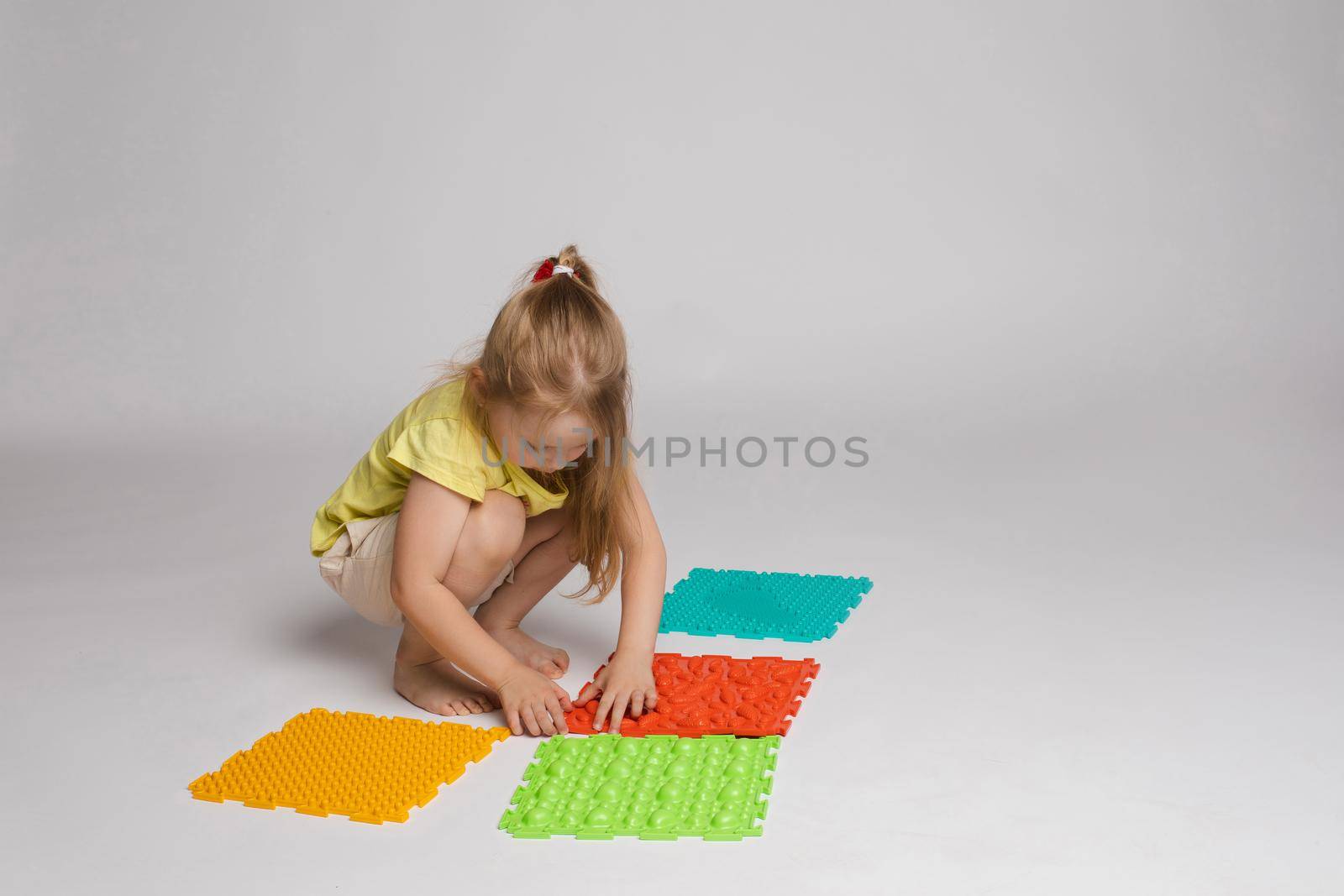 Stock photo of a child playing with colorful bright rubber pads for improving and developing fine motor skills on the floor. She is sitting on her haunches in studio.