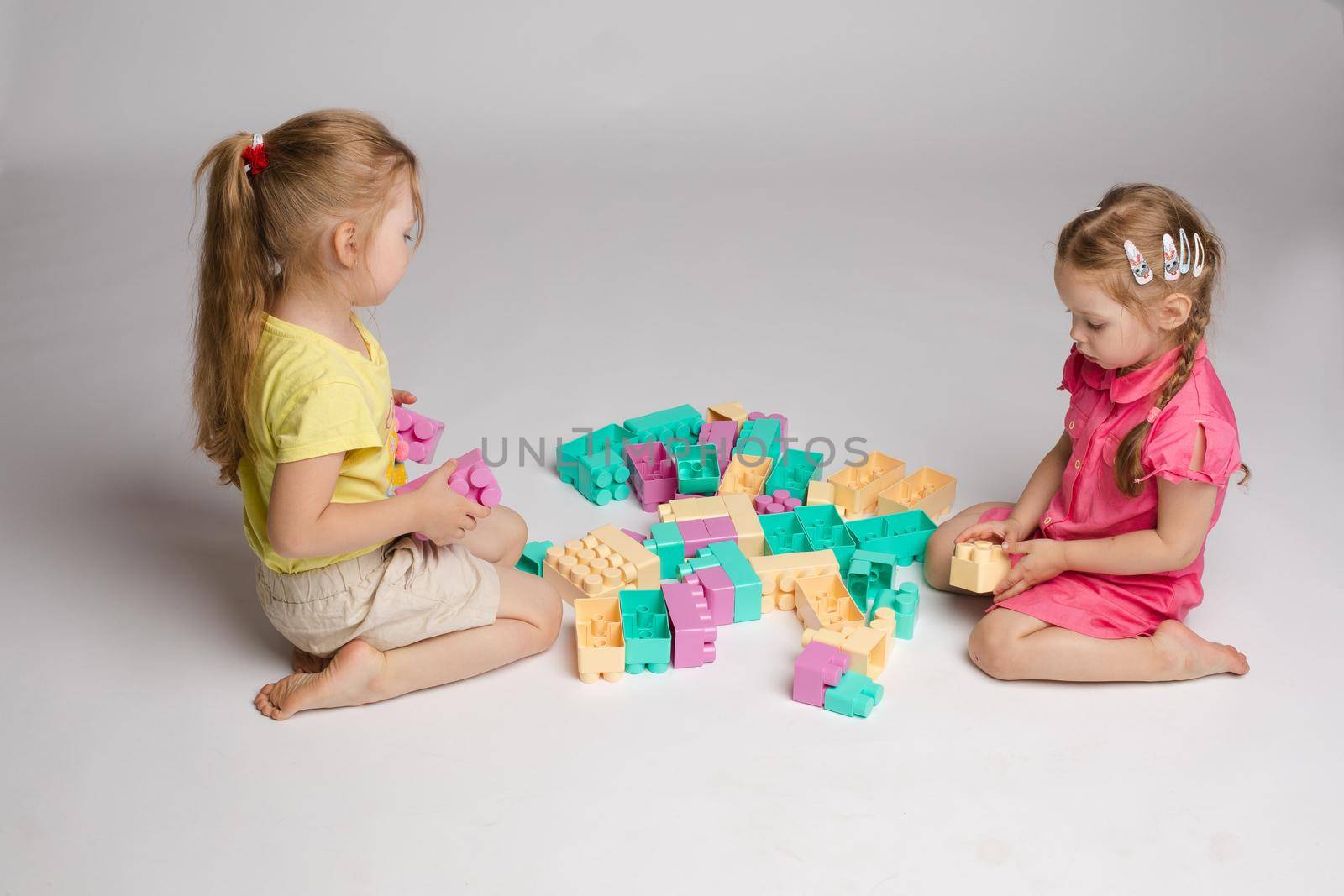 Two girls sitting on floor and playing with building blocks by StudioLucky