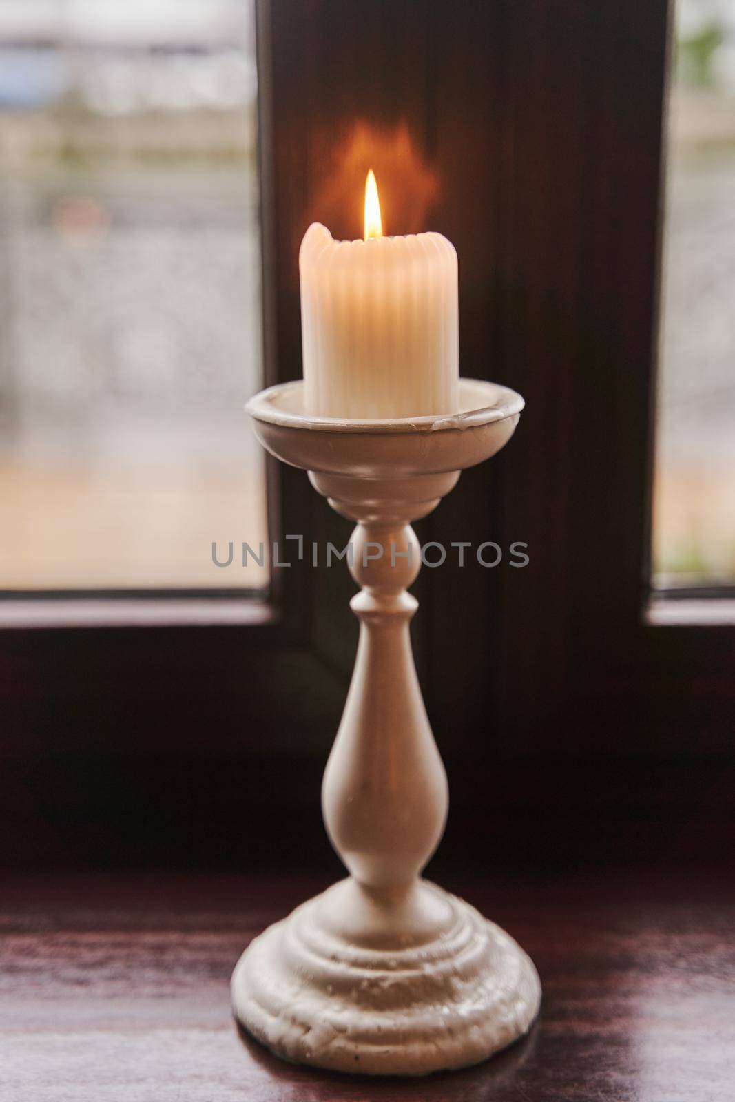 A burning candle in a candlestick stands on the windowsill. High quality photo