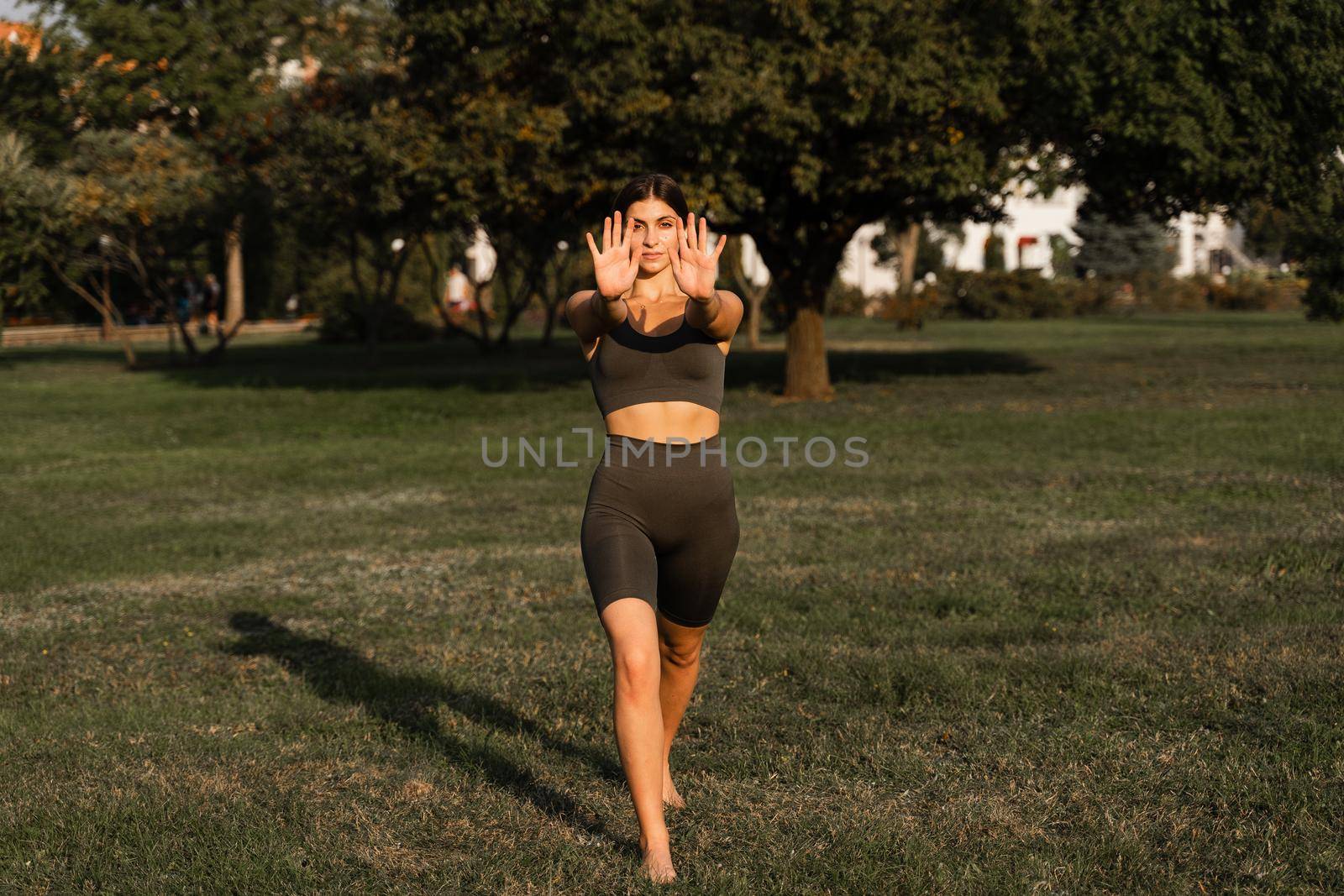 Qigong meditation exercises outdoor. Fit asian girl does chinese training on the green grass in the park. by Rabizo