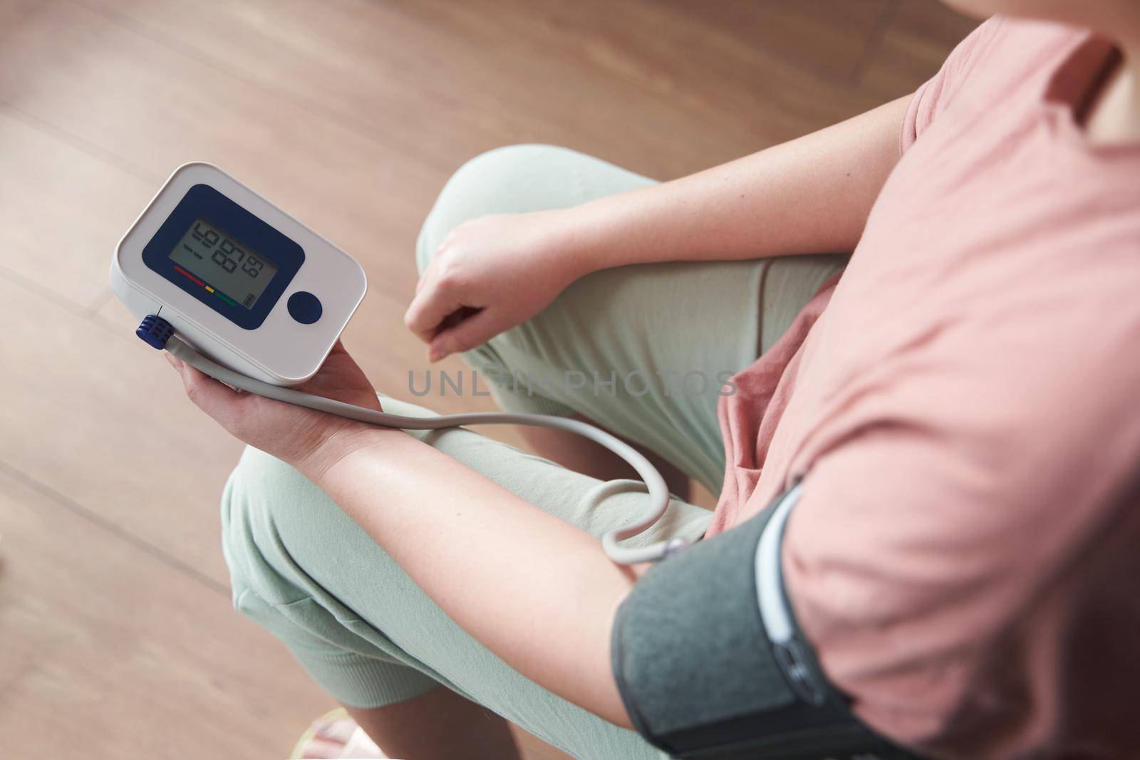 Selective focus girl is taking care for health with hearth beat monitor and blood pressure and heart rate monitor with digital pressure gauge. Health care and Medical concept. The topic of high blood pressure is hypertension disease. Close-up macro young caucasian woman hands using automatic tonometer to check pressure at home in bedroom on bed.