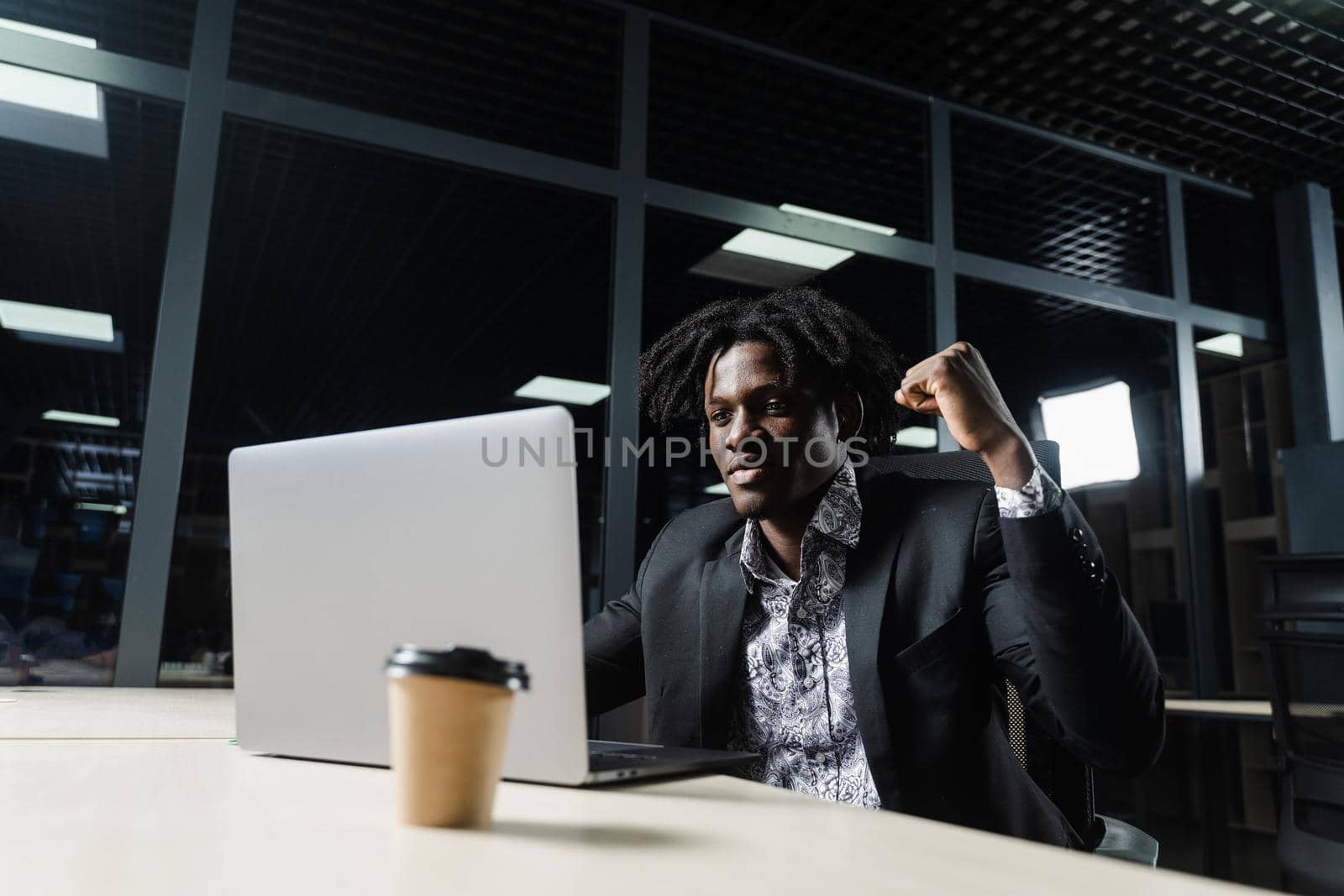 Happy black man with clenched fists is looking on the screen of laptop and rejoice finishing his job. by Rabizo