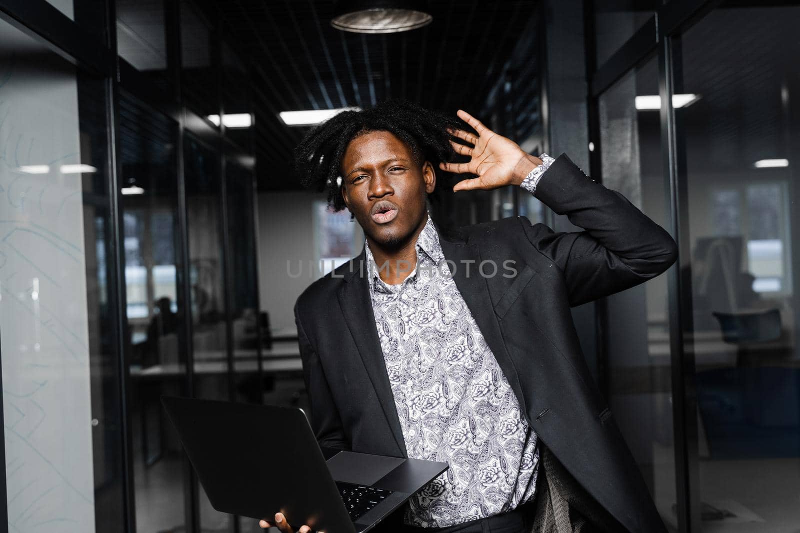 Surprised black man with laptop in the office. Shocked emotional handsome african business man in coworking space