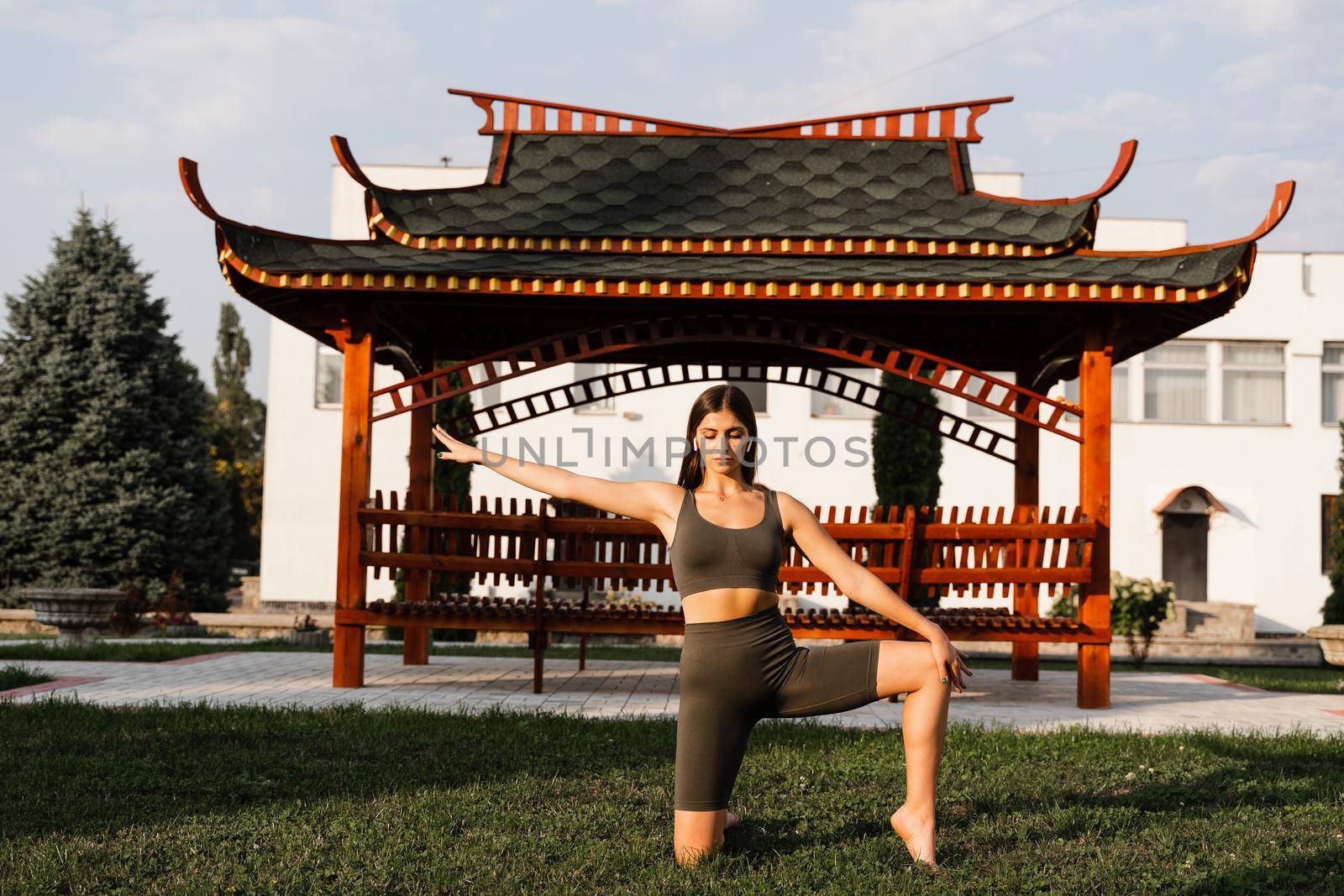 Qigong chinese meditation and sport training outdoor. Fit asian girl is meditating outdoor near chinese arbor. by Rabizo