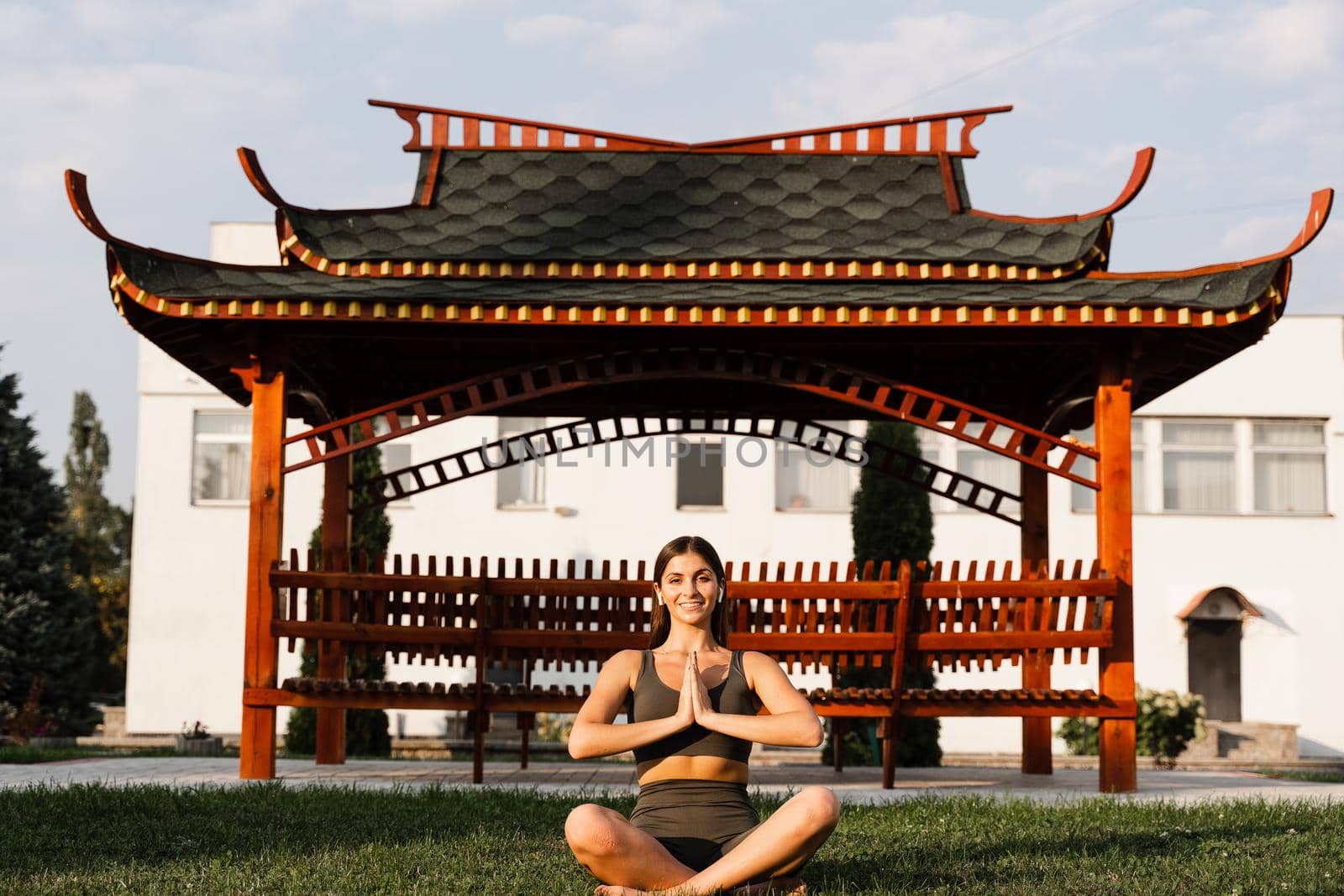 Praying and meditation in lotus position. Fit girl is sitting and meditating outdoors near chinese gazebo