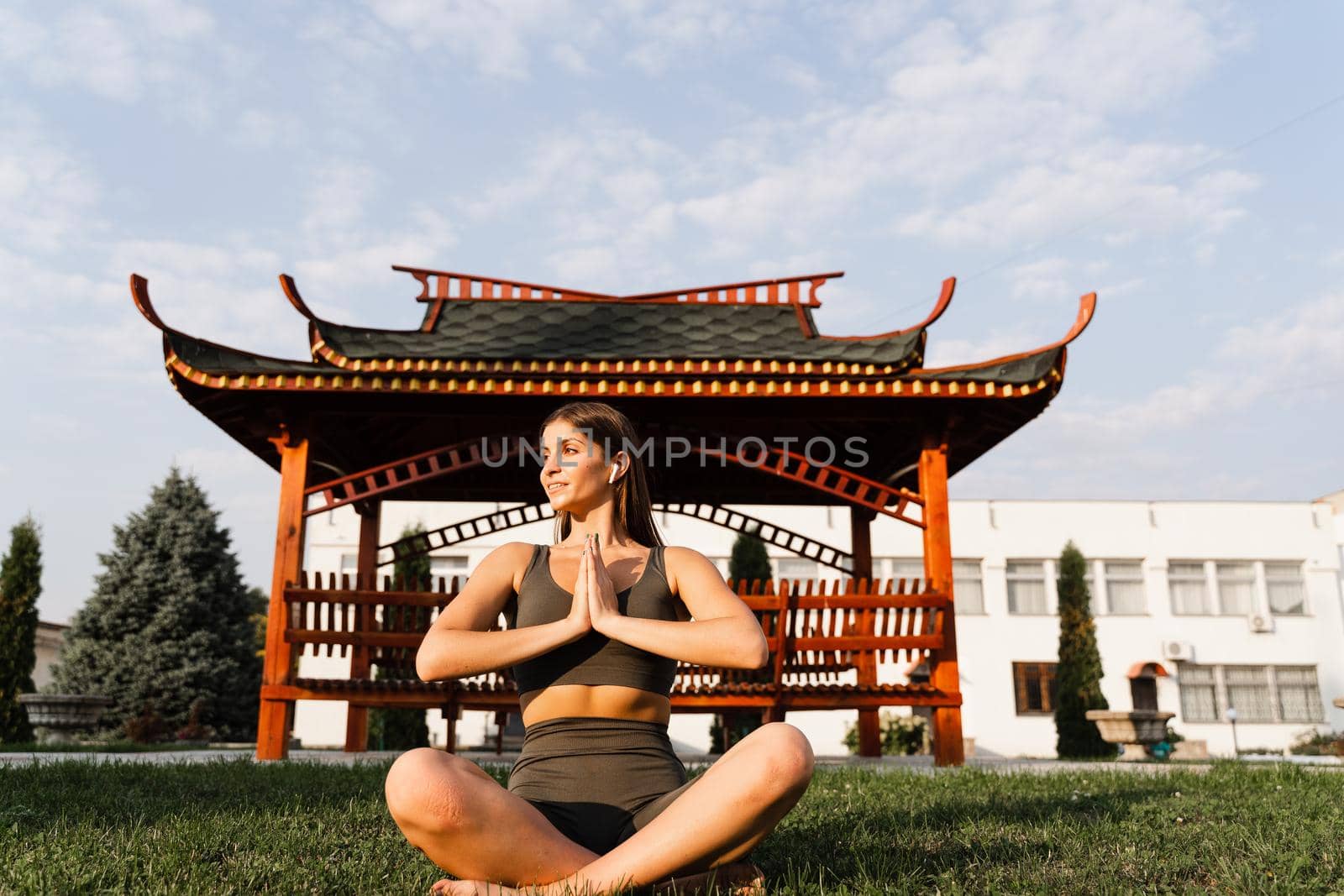Praying and meditation in lotus position. Fit girl is sitting and meditating outdoors near chinese gazebo