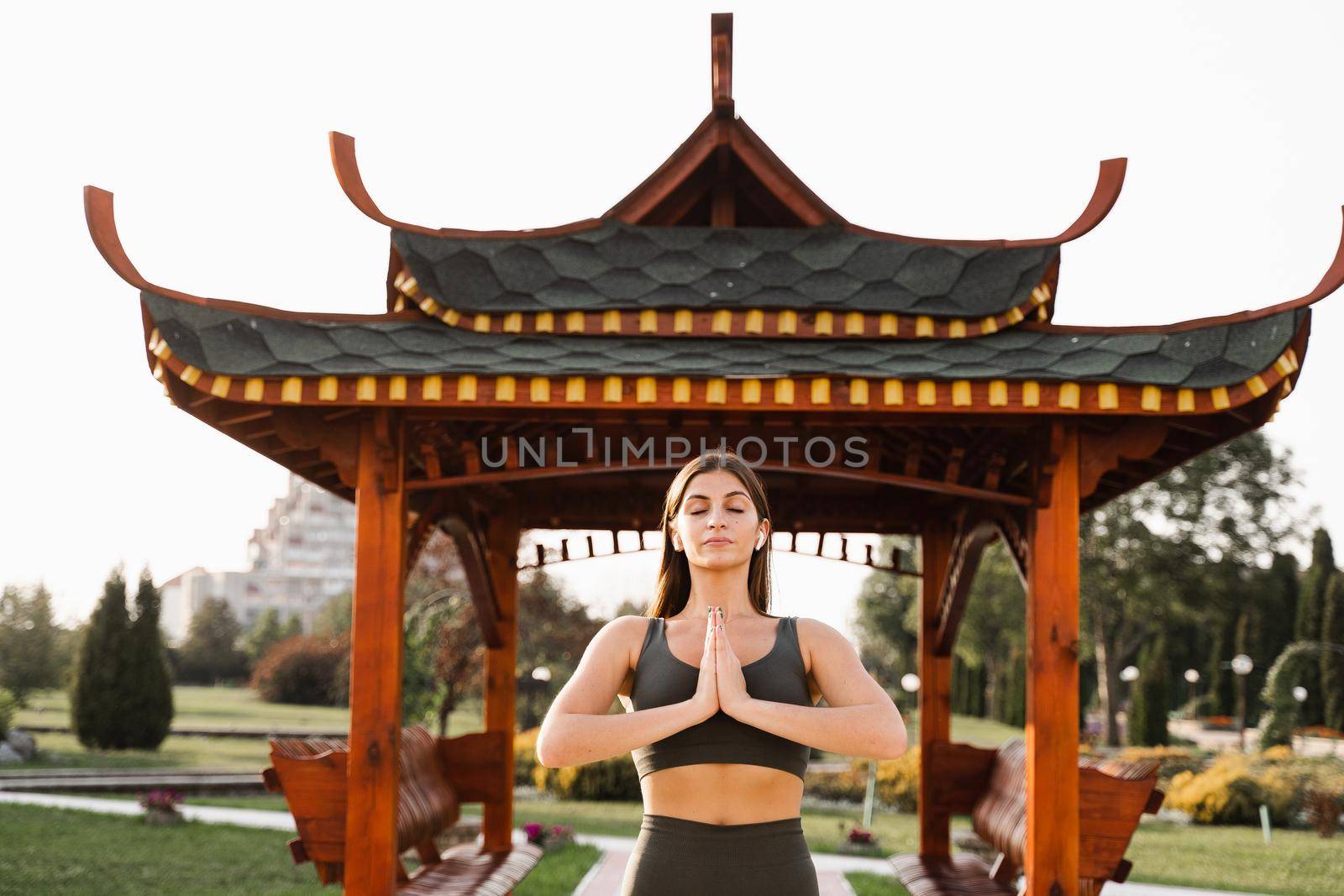 Qigong chinese meditation and sport training outdoor. Fit asian girl is meditating outdoor near chinese arbor. by Rabizo