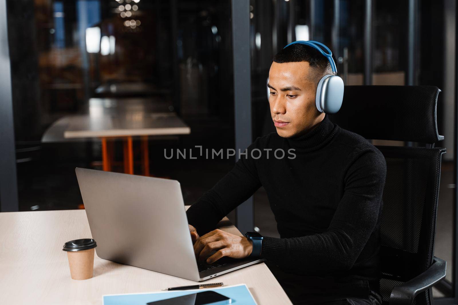 Asian man in headphones working online and listen to music in office. Asian handsome guy with laptop in coworking space. by Rabizo