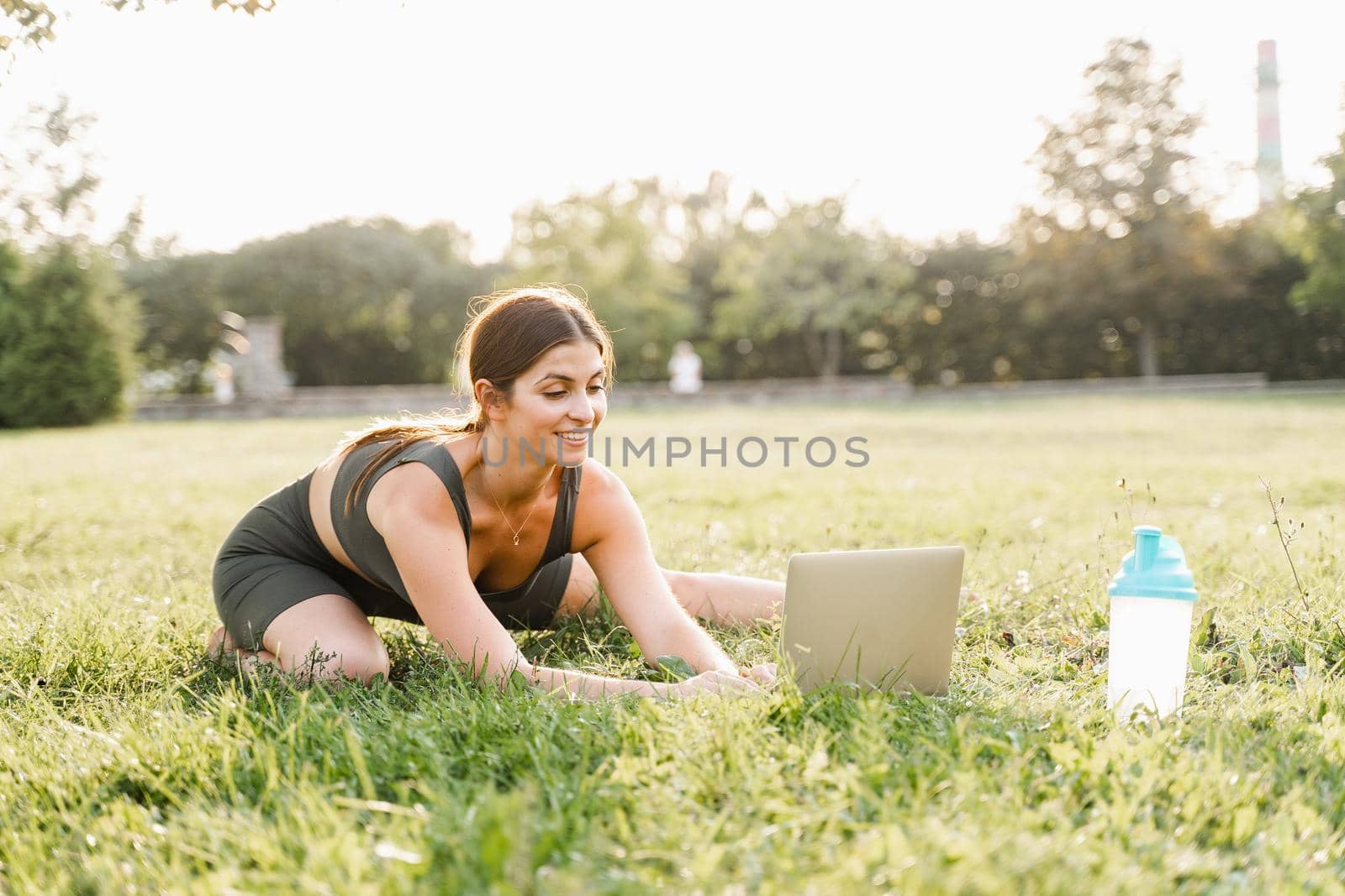 Fit girl with laptop on the green grass. Fitness trainer is chatting online with clients and explain exercises. Sport lifestyle. by Rabizo