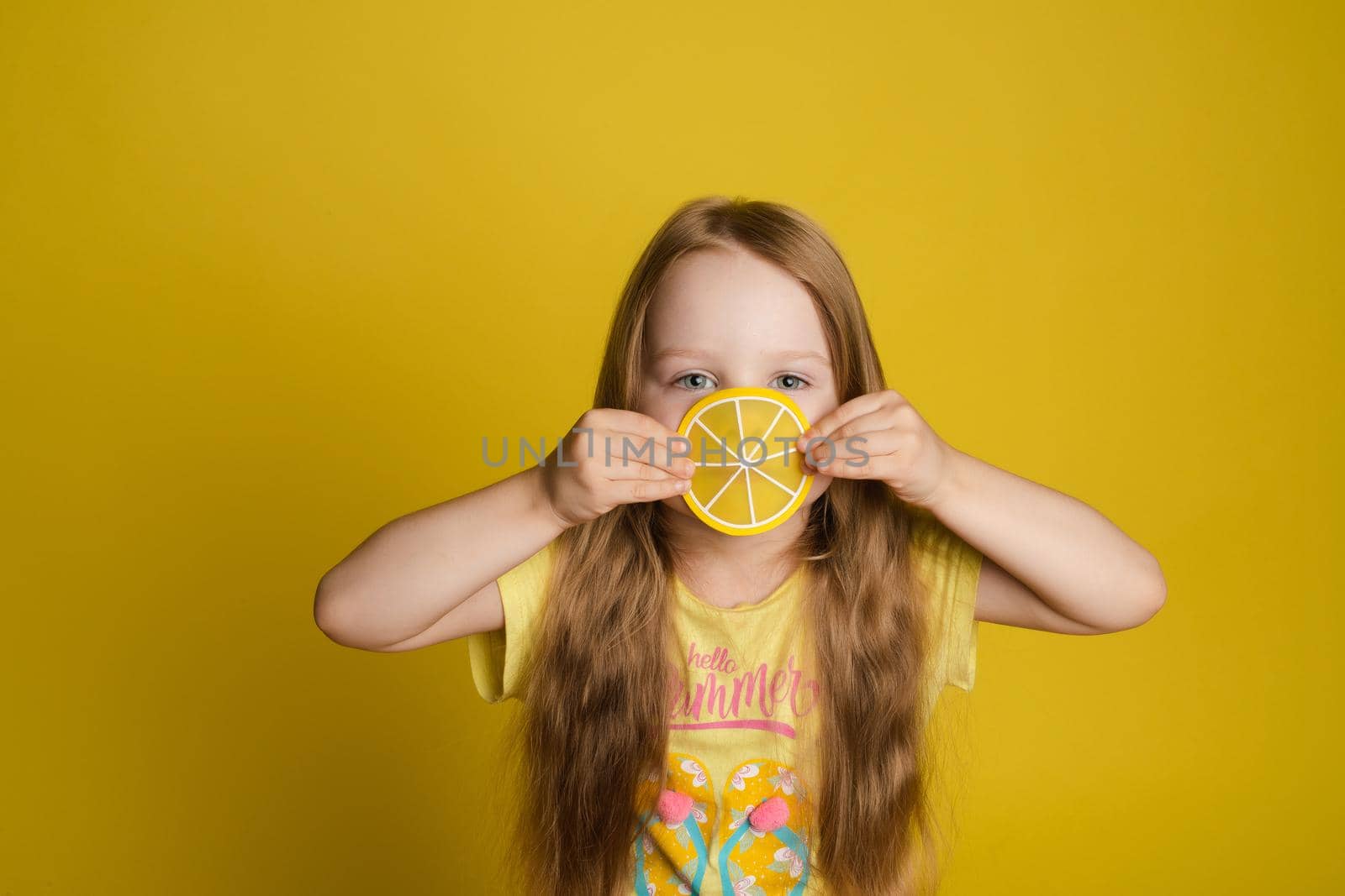 Portrait of smiling little girl holding slice of lemon near eye looking at camera medium close-up by StudioLucky