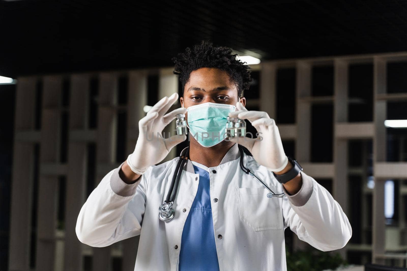 Black doctor with 3 doses of vaccine. Booster vaccination. African doctor in medical mask is holding vaccines in hand. by Rabizo