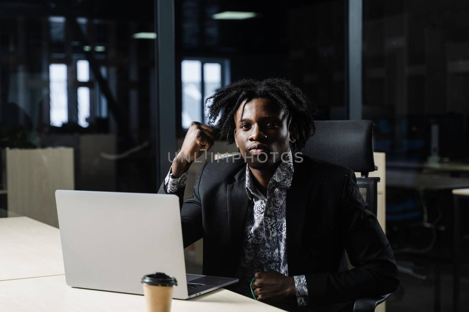 Happy black man clenched fists and rejoice finishing his online job on laptop. Working online in coworking space