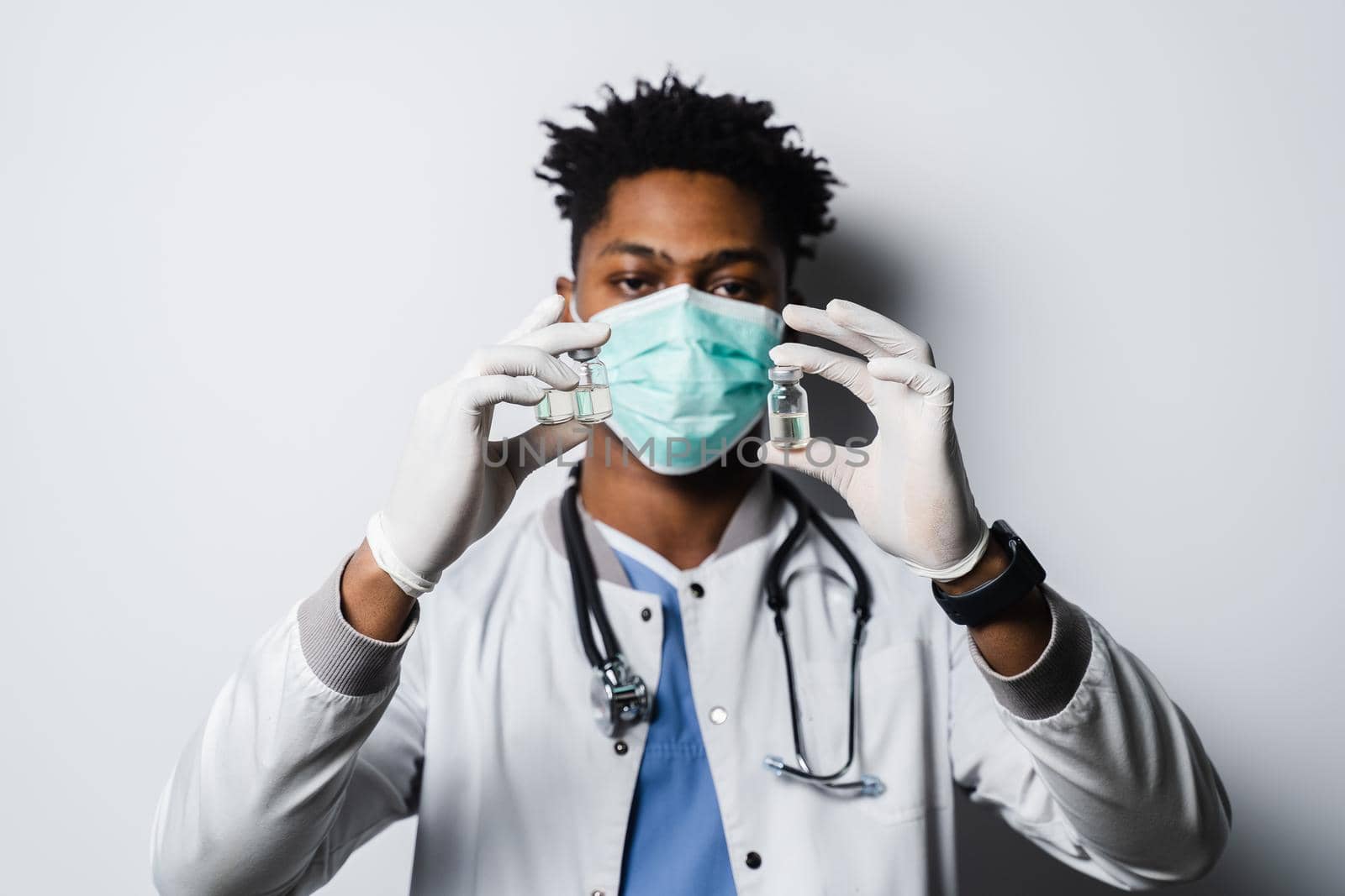 Handsome African doctor with coronavirus covid-19 vaccine. Black doctor in medical mask is holding vaccine on white background. by Rabizo