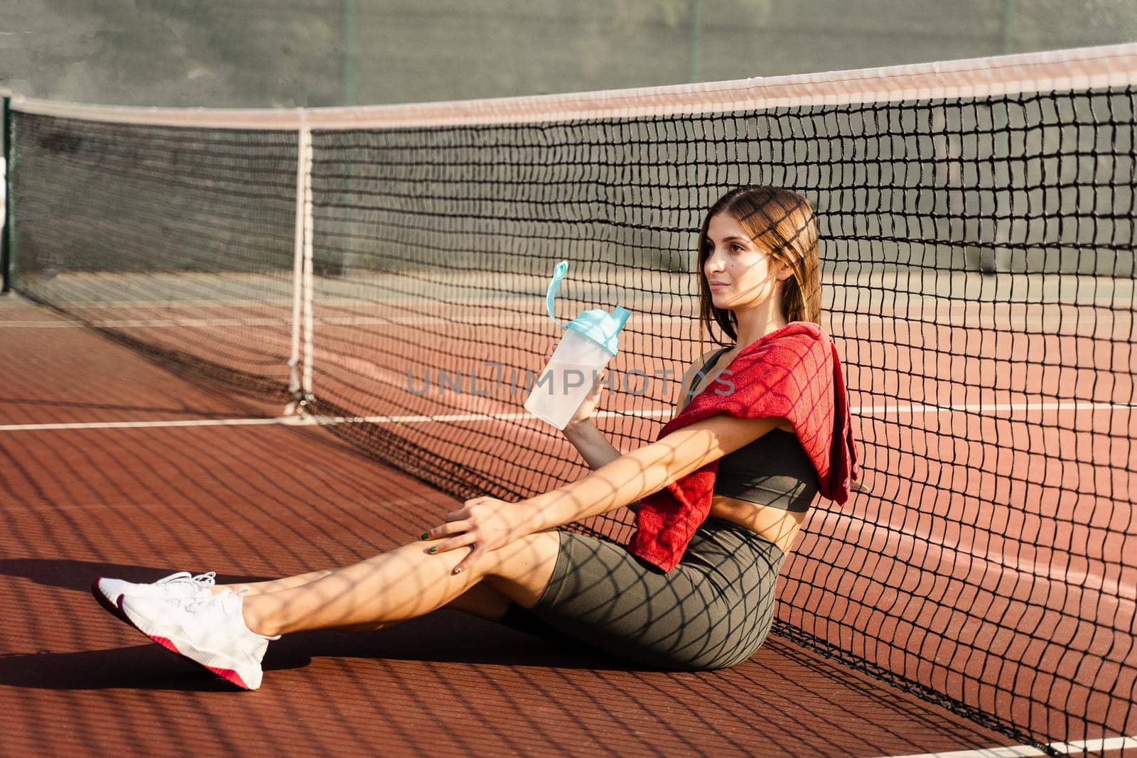Athletic fit Asian girl drinking water from a bottle. Rest after training on the tennis court. by Rabizo