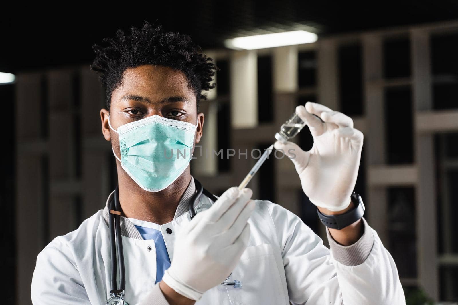 African doctor in a medical mask prepares to inject coronavirus covid-19 vaccine. Black doctor in white medical robe with syringe for making vaccination. by Rabizo