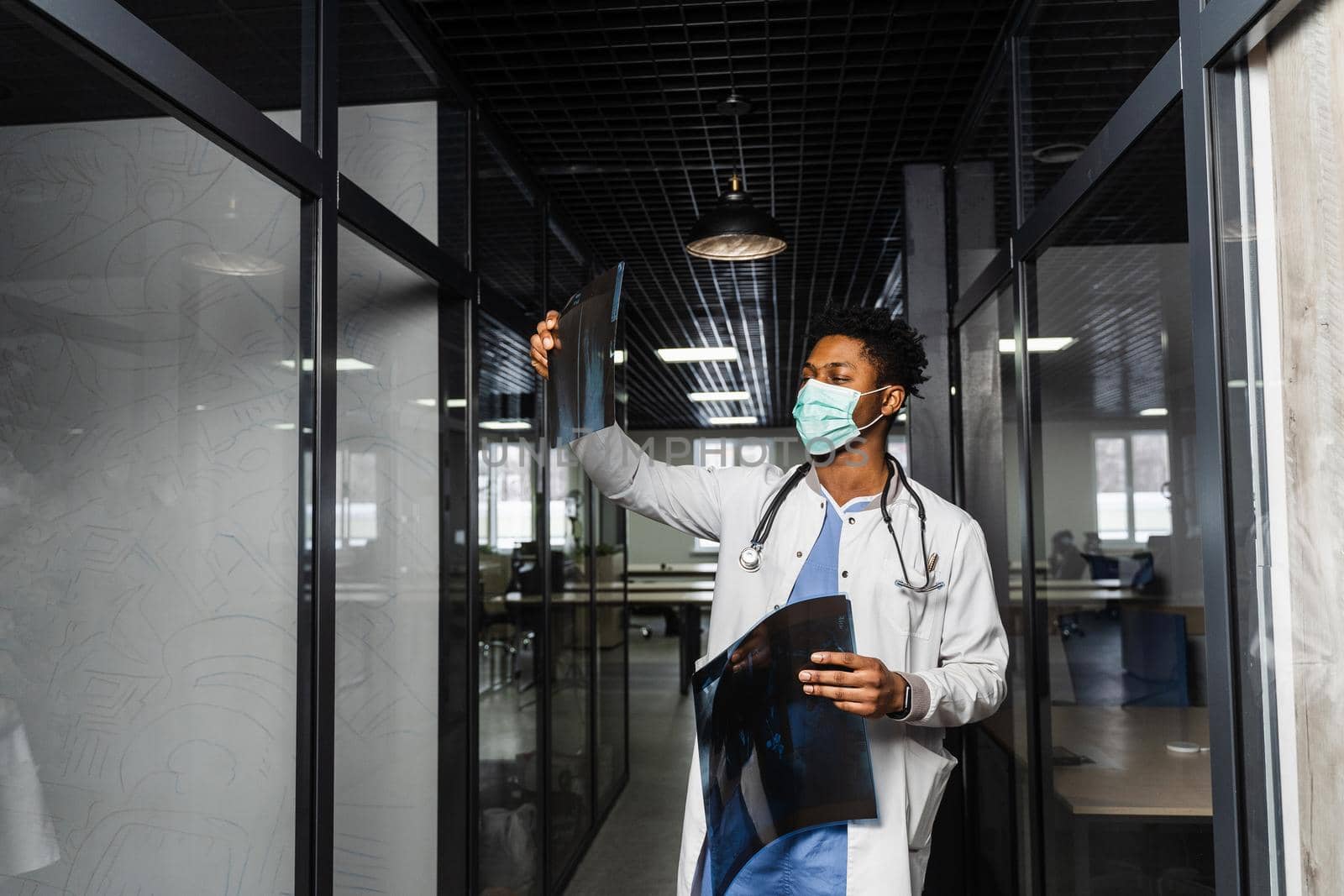 African doctor examines x-rays in a medical clinic. Black student in medical mask is studying and looking at ct scans. by Rabizo