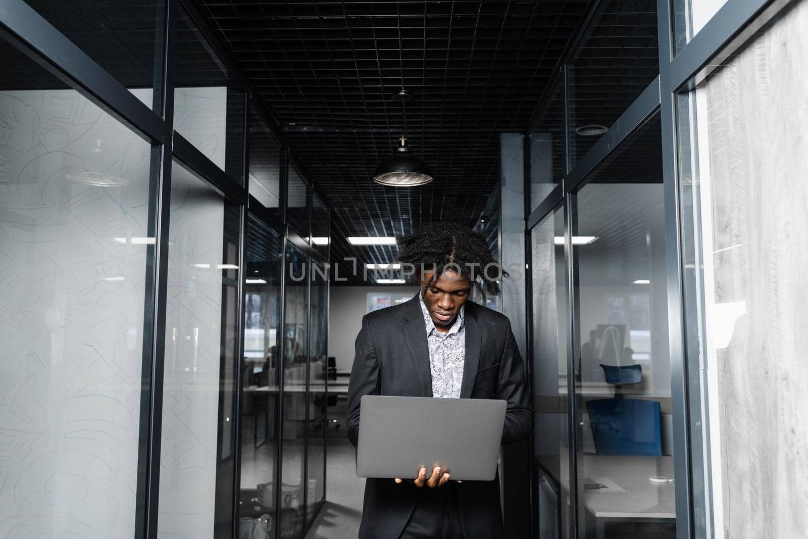 Focused young black businessman working online on laptop in office. Remote work. by Rabizo