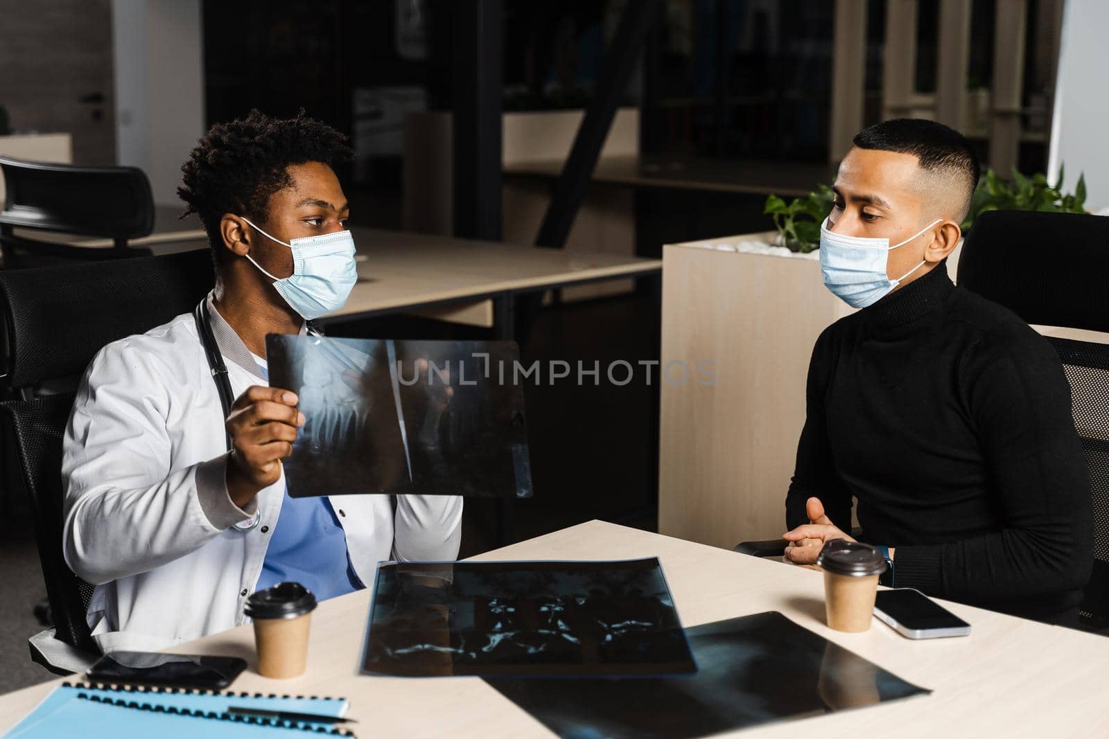 Asian patient at African doctor appointment. Fracture of the bones of foot. Black surgeon showing x-ray to patient. by Rabizo