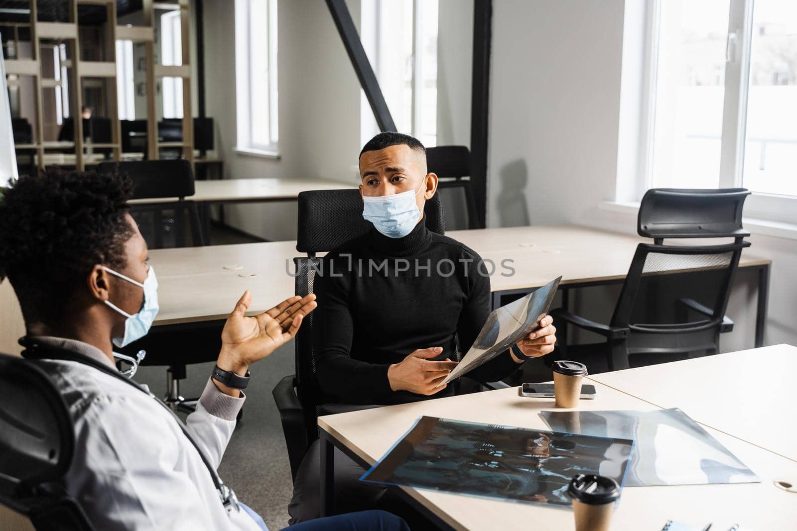 Handsome asian patient with x-ray image of fracture of foot bones at black doctor consultation. African surgeon discussing x-ray with patient