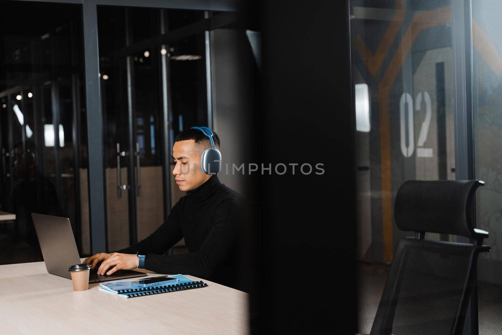 Asian man in headphones working online and listen to music in office. Asian handsome guy with laptop in coworking space