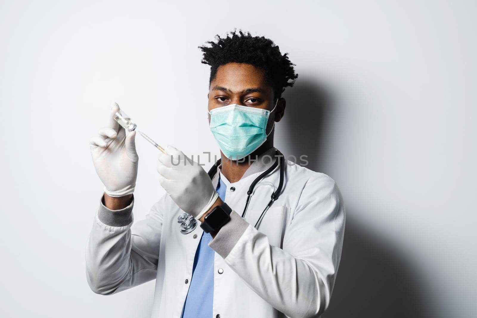 African doctor with coronavirus covid-19 vaccine in syringe. Black man in medical mask is making vaccination on white background. by Rabizo