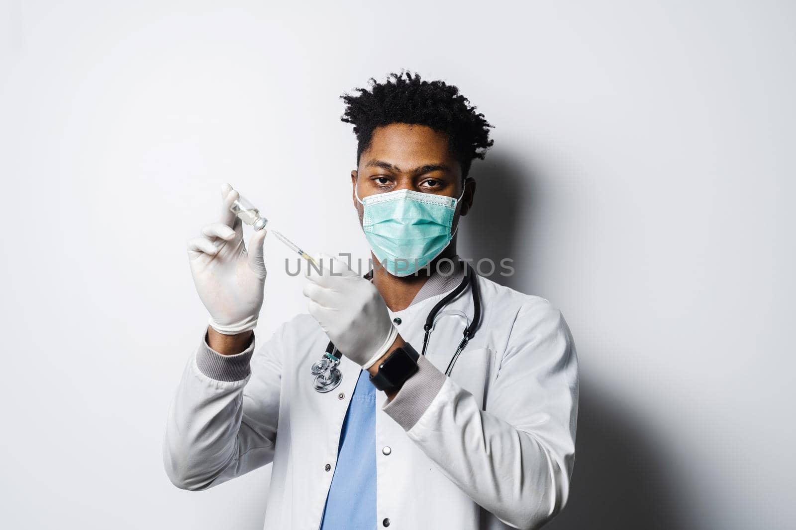 African doctor with coronavirus covid-19 vaccine in syringe. Black man in medical mask is making vaccination on white background. by Rabizo