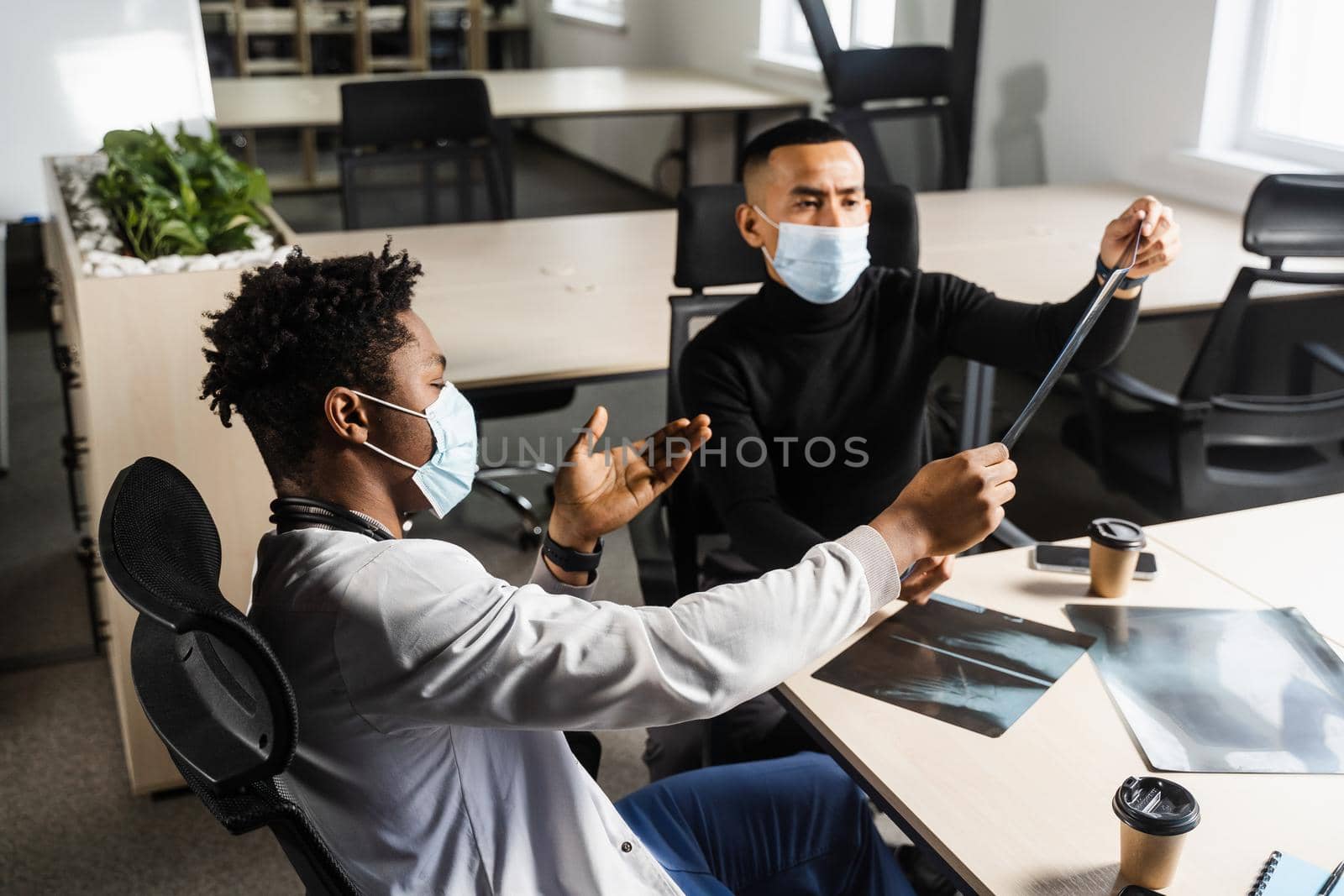 African doctor show x-ray asian patient. Black surgeon analyzing x ray and diagnosis patient in medical clinic. by Rabizo