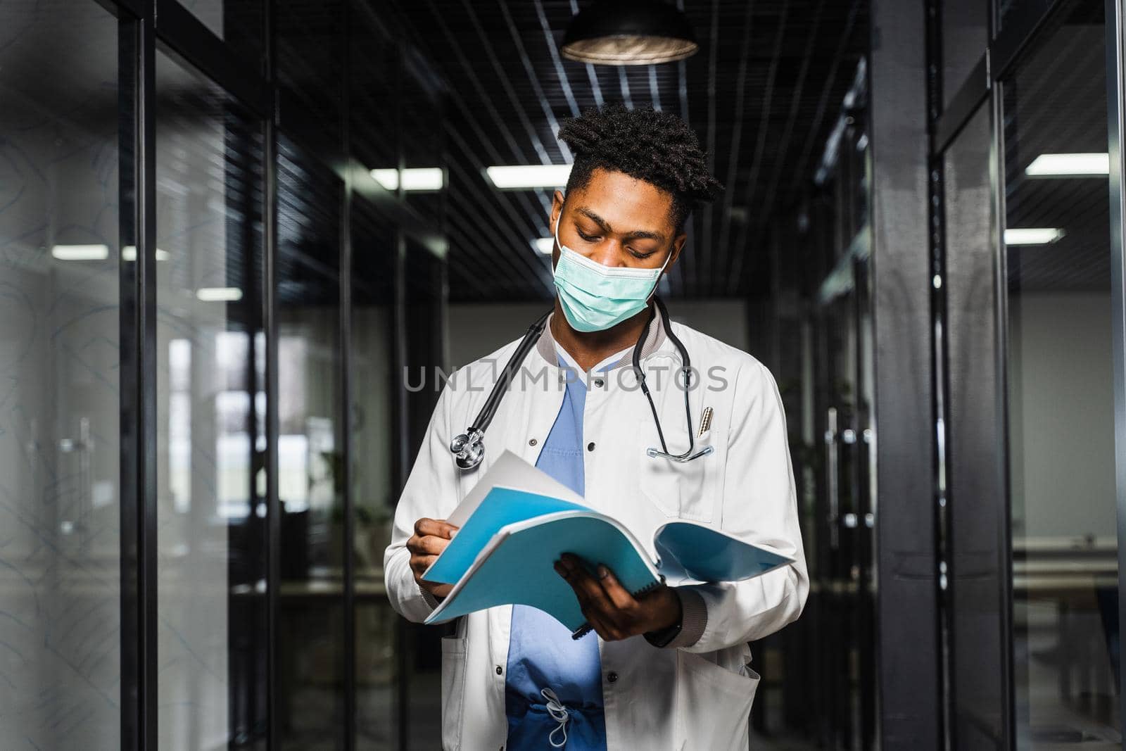 African doctor in mask with books in medical clinic. Black medical student study in university. by Rabizo