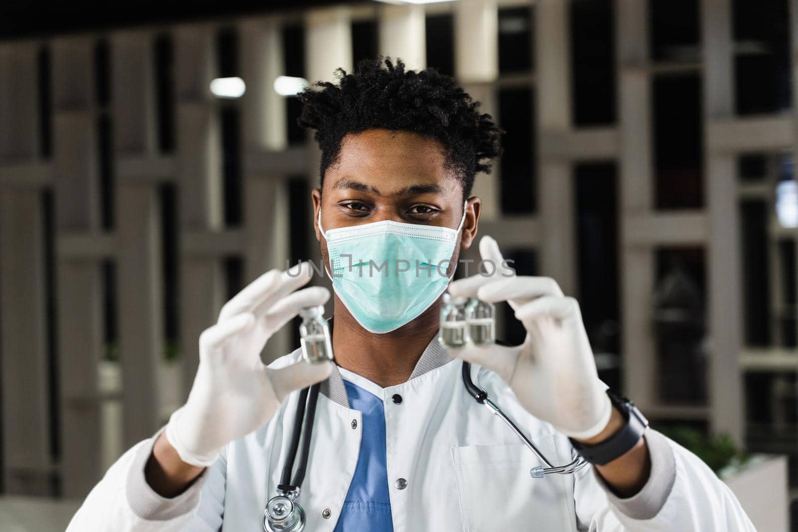 Black doctor with 3 doses of vaccine. Booster vaccination. African doctor in medical mask is holding vaccines in hand