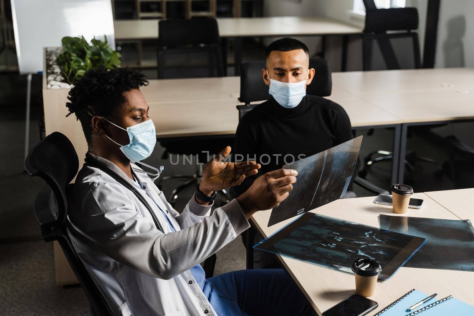 Asian patient at African doctor appointment. Fracture of the bones of foot. Black surgeon showing x-ray to patient