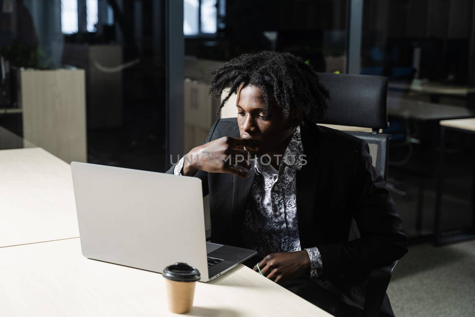 Black IT programmer is working on laptop in coworking space. Handsome african man with laptop in the office. by Rabizo
