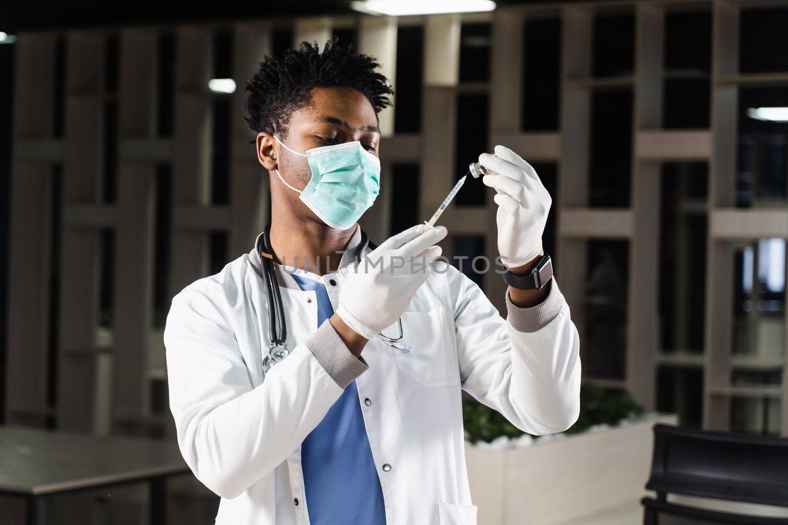 African doctor in a medical mask prepares to inject coronavirus covid-19 vaccine. Black doctor in white medical robe with syringe for making vaccination