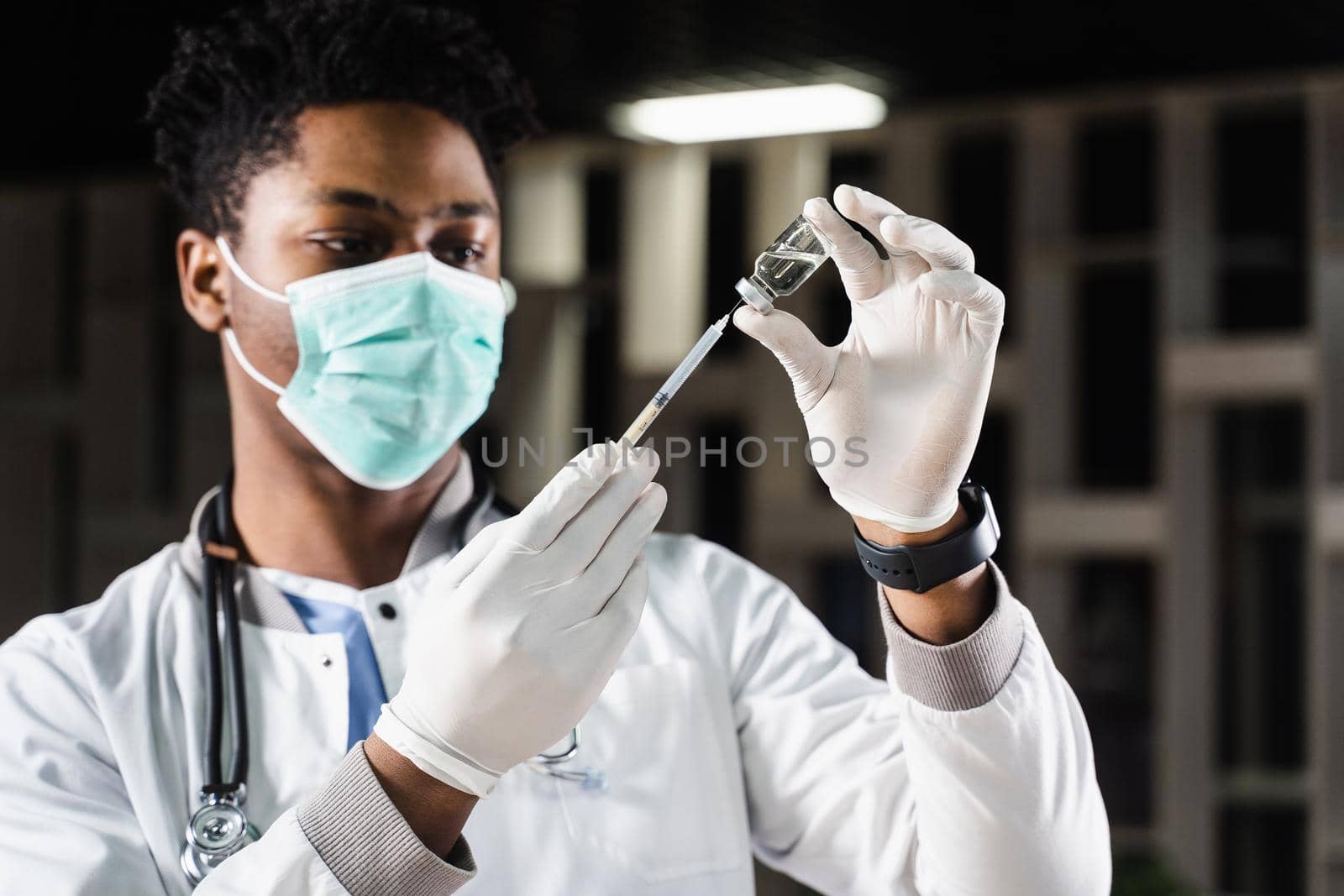 African doctor in a medical mask prepares to inject coronavirus covid-19 vaccine. Black doctor in white medical robe with syringe for making vaccination. by Rabizo