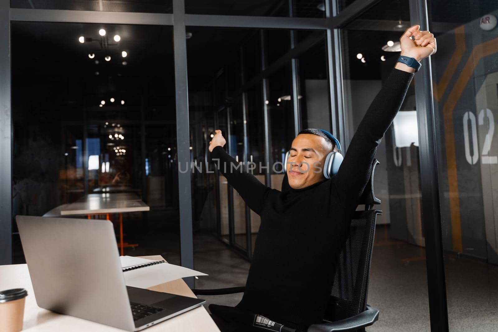 Tired and sleepy Asian man raises his hands up and yawns at the workplace. Work online overtime. Man wants to sleep at work