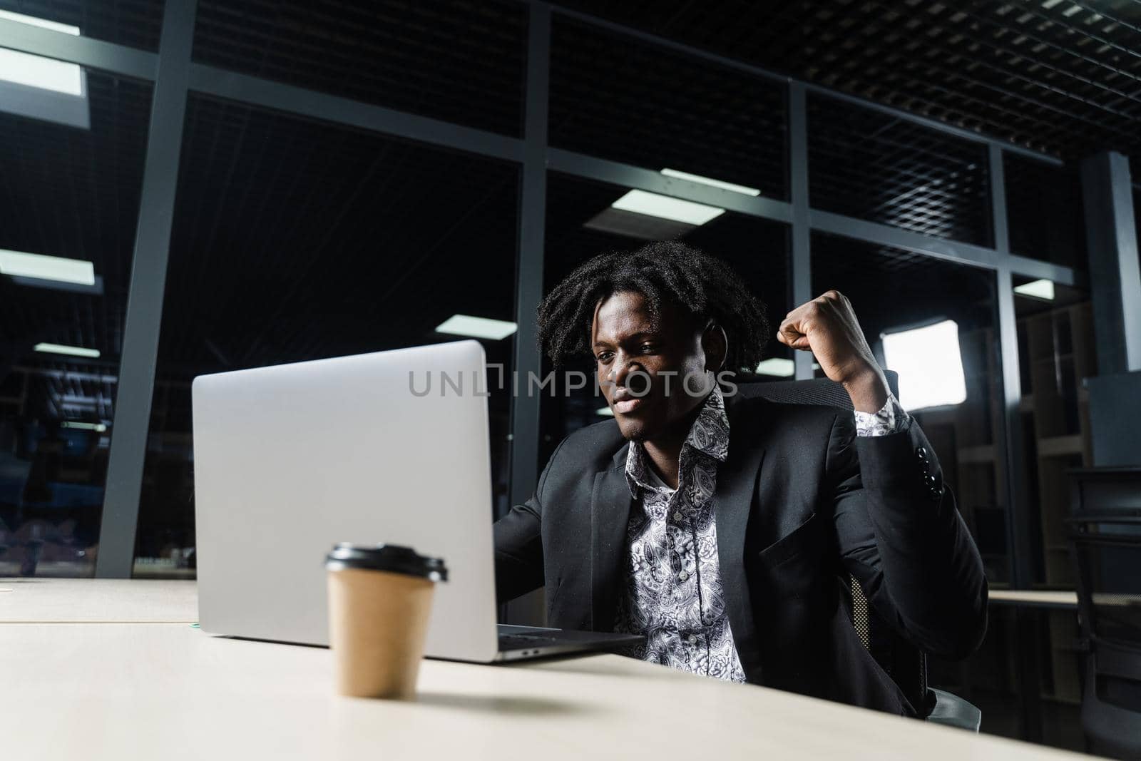 Happy black man with clenched fists is looking on the screen of laptop and rejoice finishing his job. by Rabizo