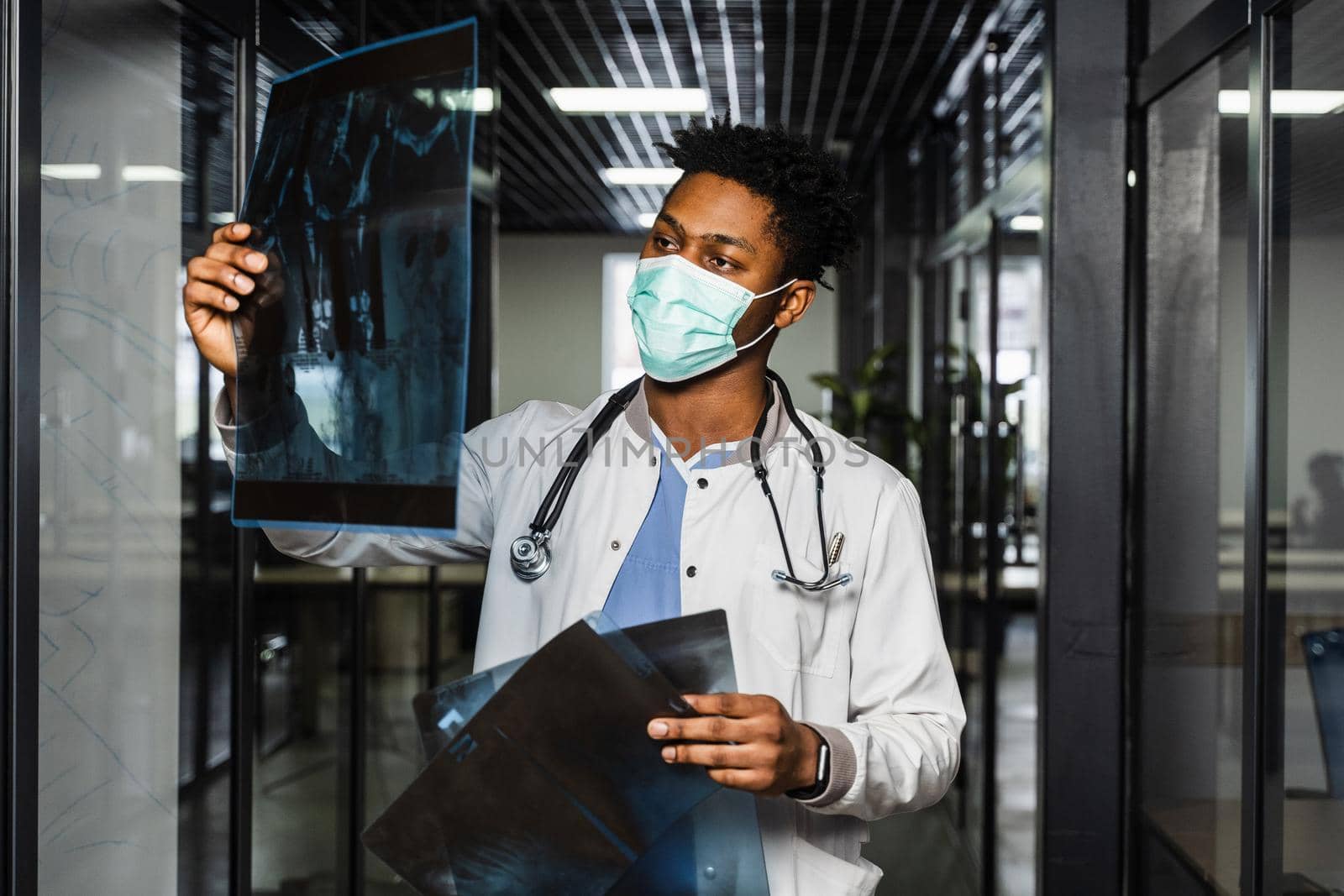 African doctor examines x-rays in a medical clinic. Black student in medical mask is studying and looking at ct scans. by Rabizo