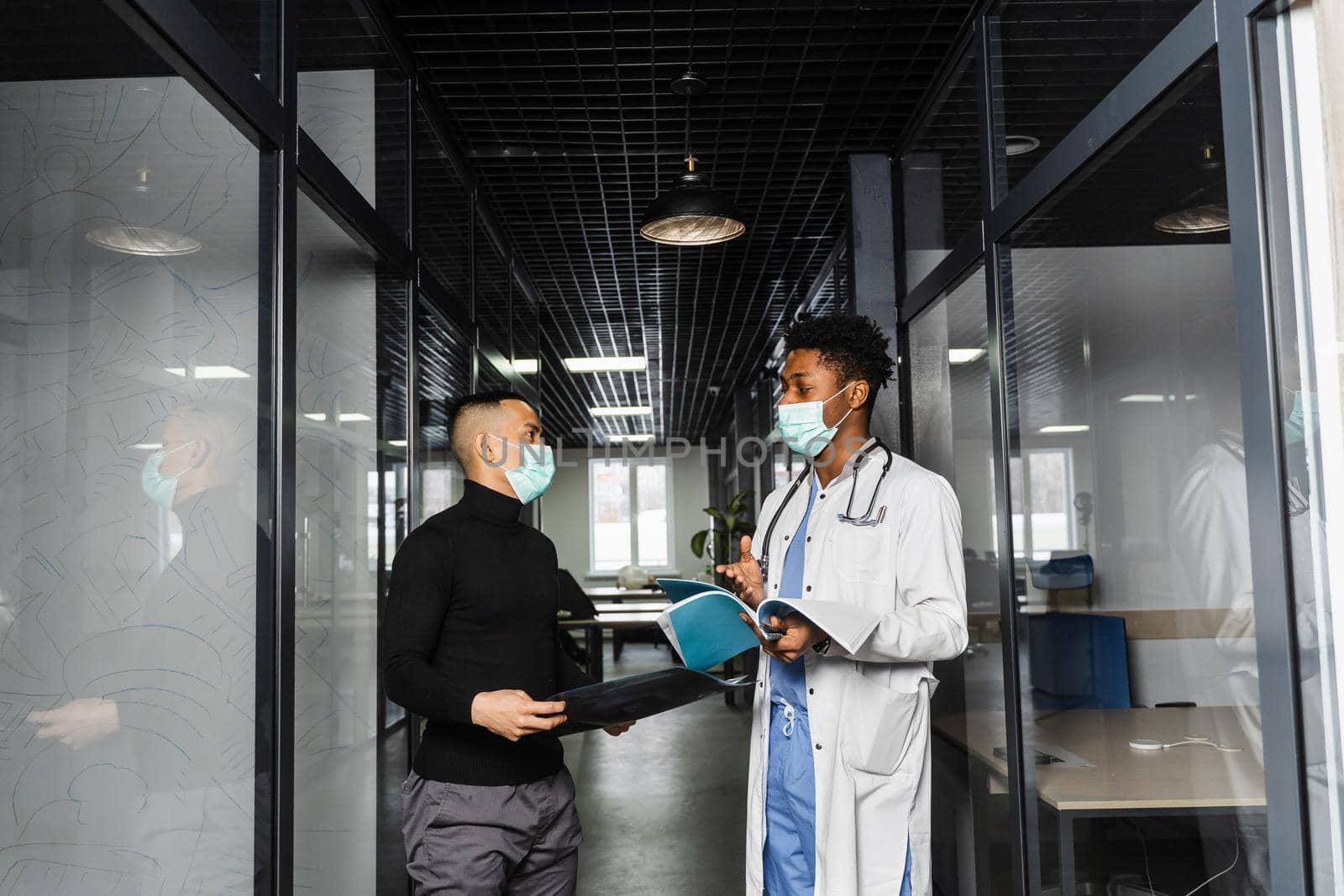 Discussion and consultation between black doctor and patient in medical clinic. African surgeon treats Asian handsome man