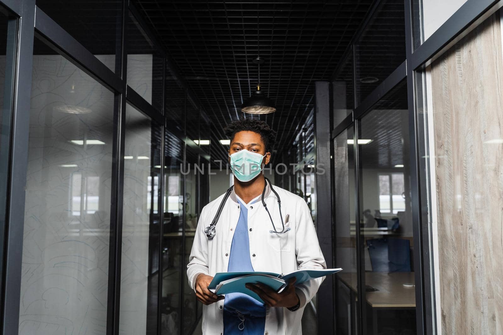 Black medical student reads books and prepares for an exam. African in a medical robe and mask looks at the notes. by Rabizo