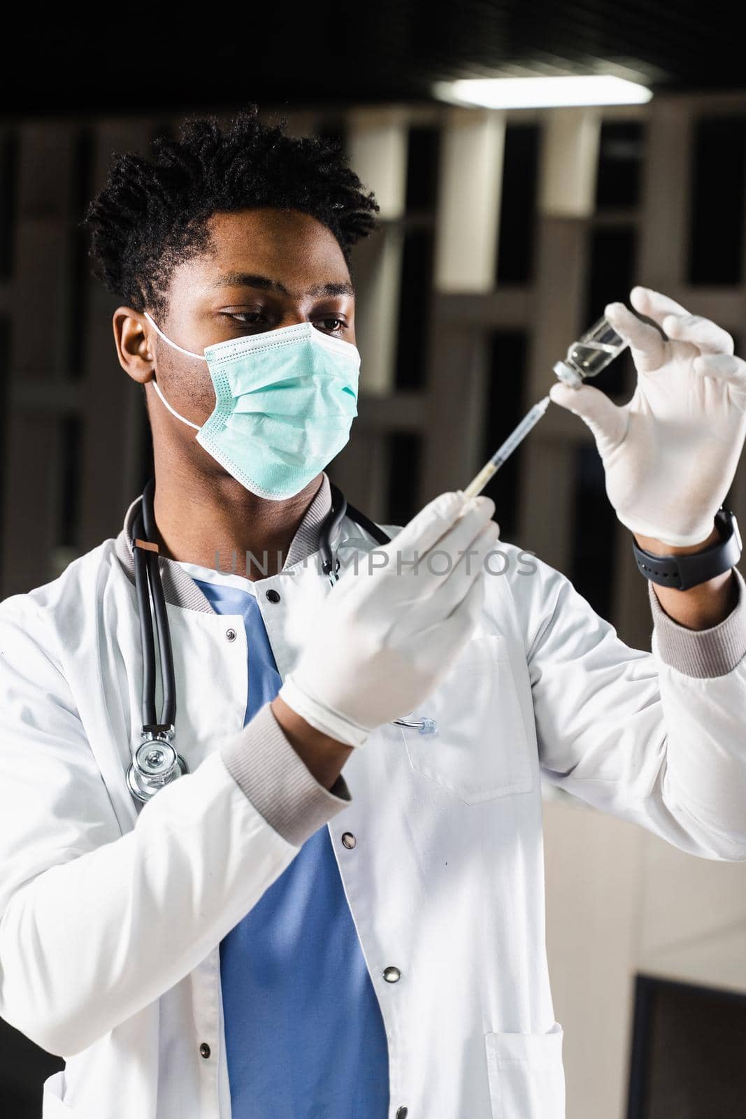 African doctor in a medical mask prepares to inject coronavirus covid-19 vaccine. Black doctor in white medical robe with syringe for making vaccination. by Rabizo